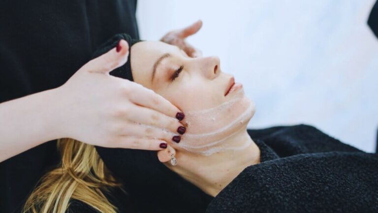 Young woman receives a relaxing facial treatment, with hands gently massaging her head. Her expression is calm, conveying a sense of tranquility.