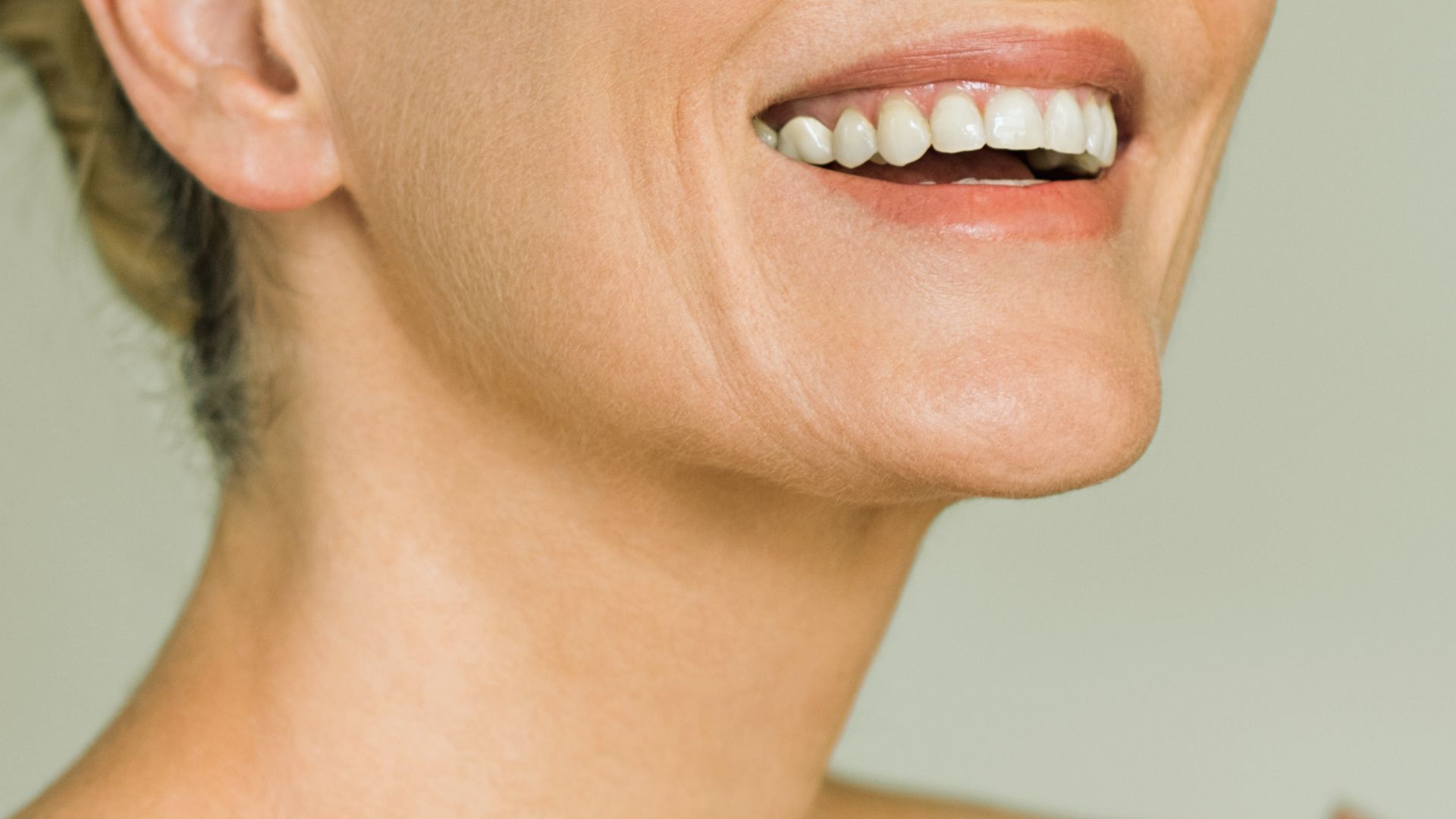Close-up of a woman's smiling mouth and jawline, highlighting her straight, white teeth and smooth skin, conveying happiness and warmth.