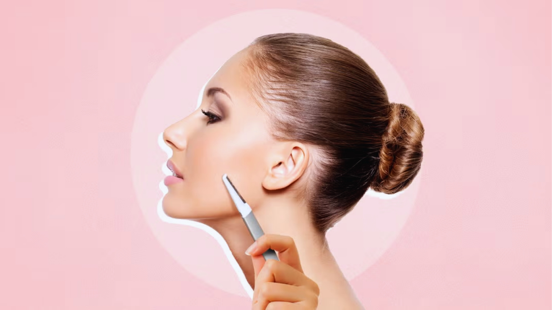 A profile of a woman with sleek hair in a bun holding a facial tool near her jawline against a pink background, conveying a sense of elegance and care.