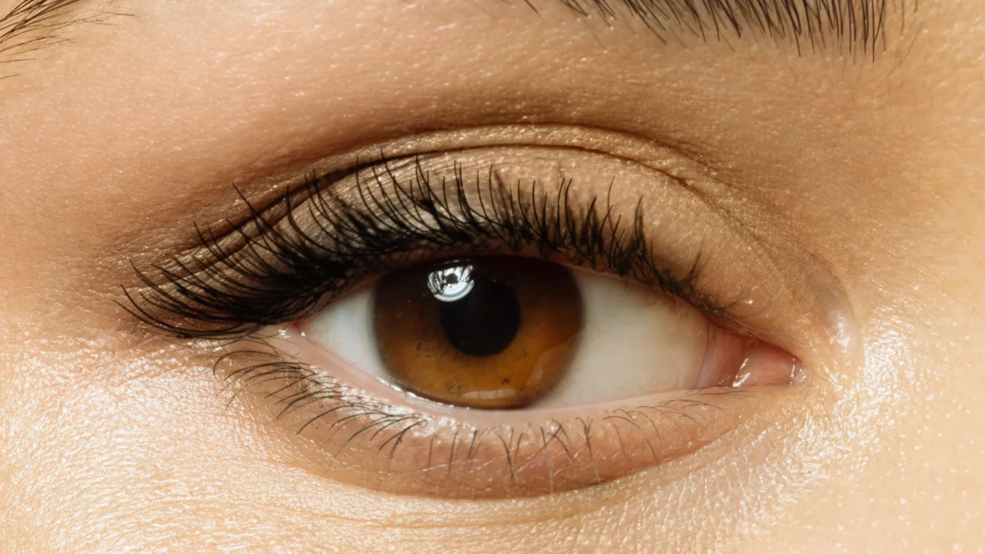 Close-up of a brown eye with long lashes and well-defined eyebrows. The skin appears smooth and natural, conveying a sense of focus and clarity.