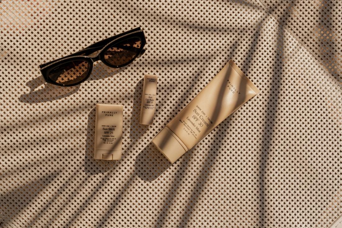 A pair of sunglasses, a bottle of sunscreen, and a tube of lip balm arranged on a flat surface, ready for sun protection.