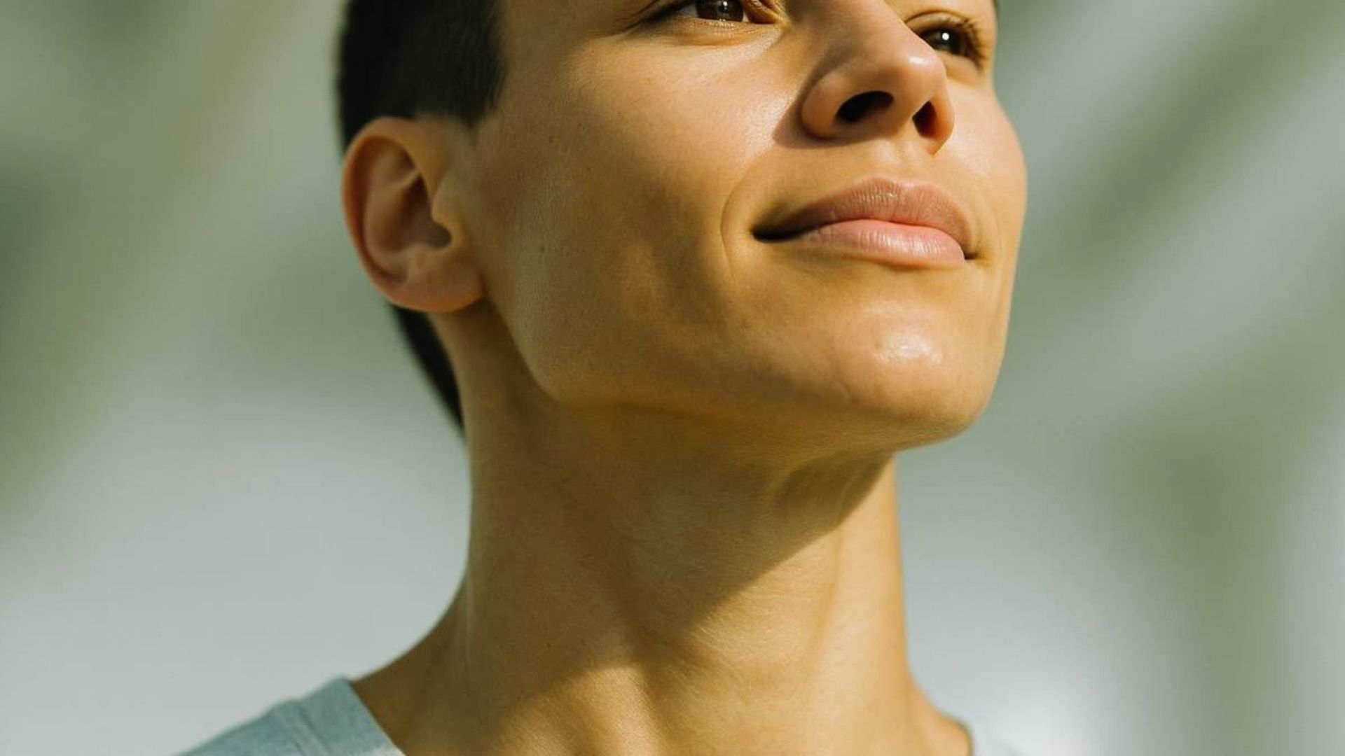 A person with short hair gazes upward with a serene expression. Soft lighting highlights their face, creating a calm and contemplative mood.