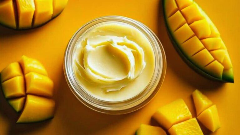 A jar of creamy mango butter sits in the center, surrounded by sliced yellow mango pieces on a matching vibrant yellow background, conveying freshness.
