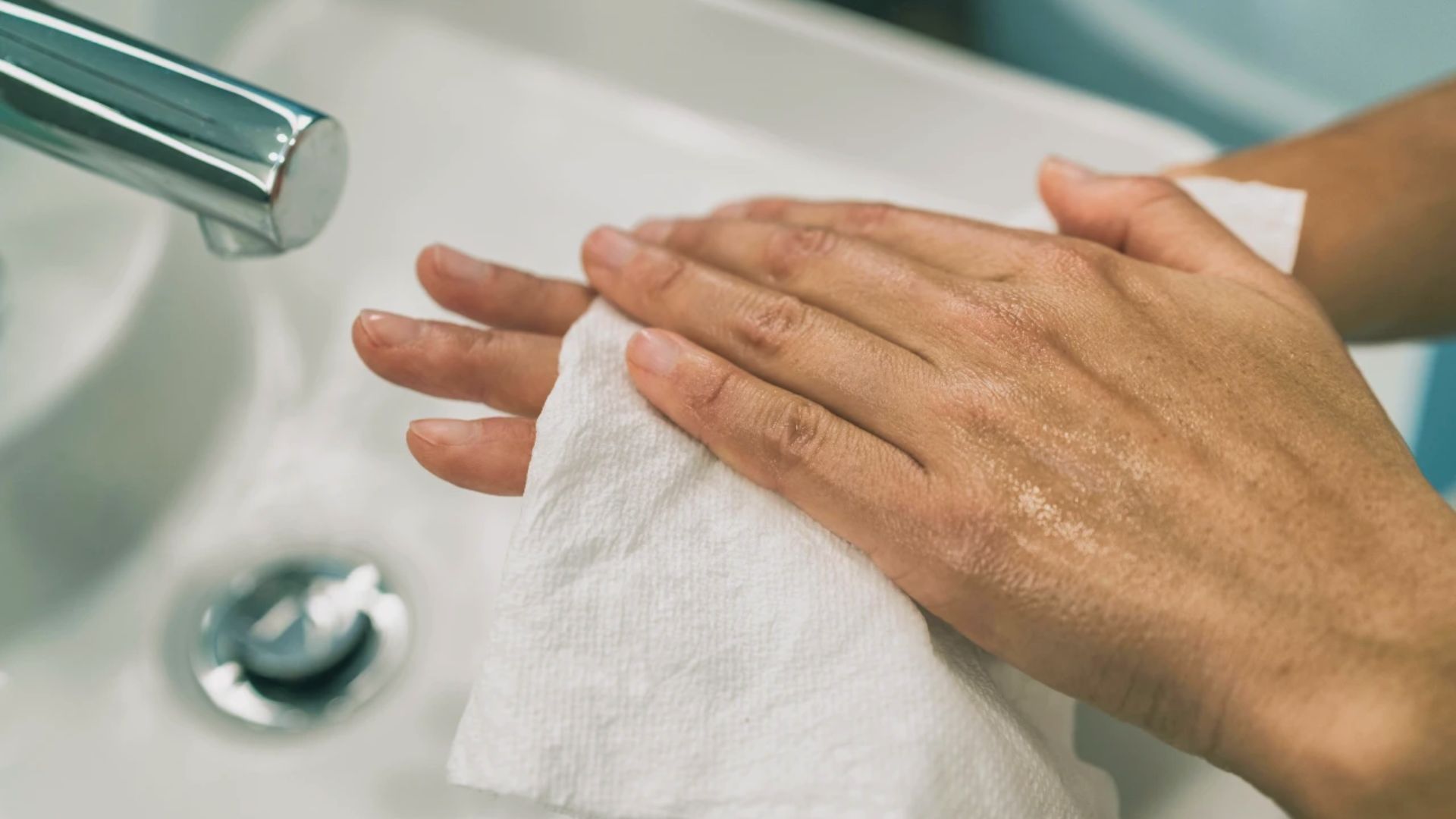 Hands drying with a white paper towel over a sink, faucet visible. The atmosphere is clean and serene, emphasizing hygiene and cleanliness.