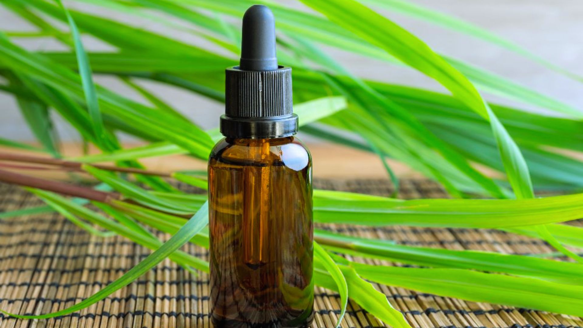 A brown glass dropper bottle sits on a woven mat with vibrant green leaves in the background, conveying a fresh, natural, and calming atmosphere.