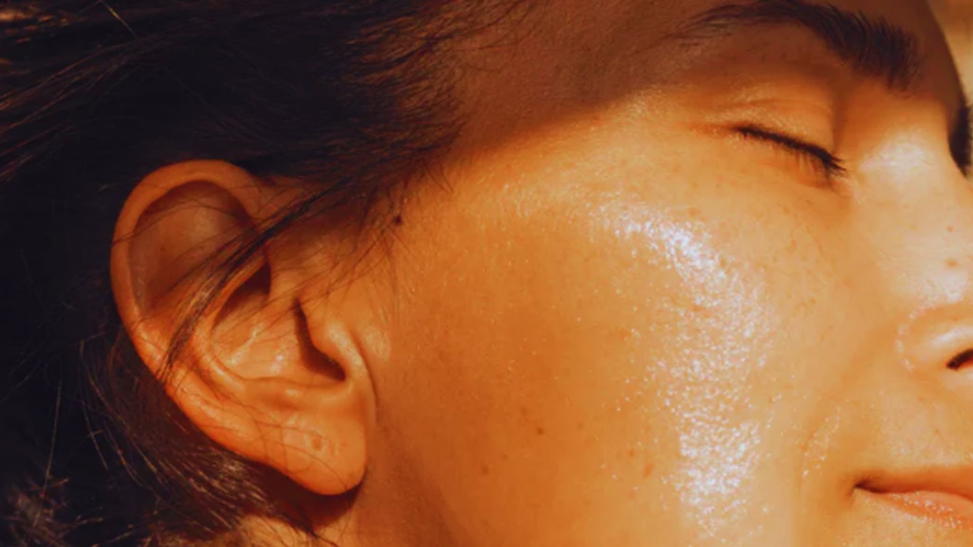 Close-up of a person's face in warm sunlight, eyes closed, with smooth, radiant skin and a serene expression, conveying calmness and relaxation.