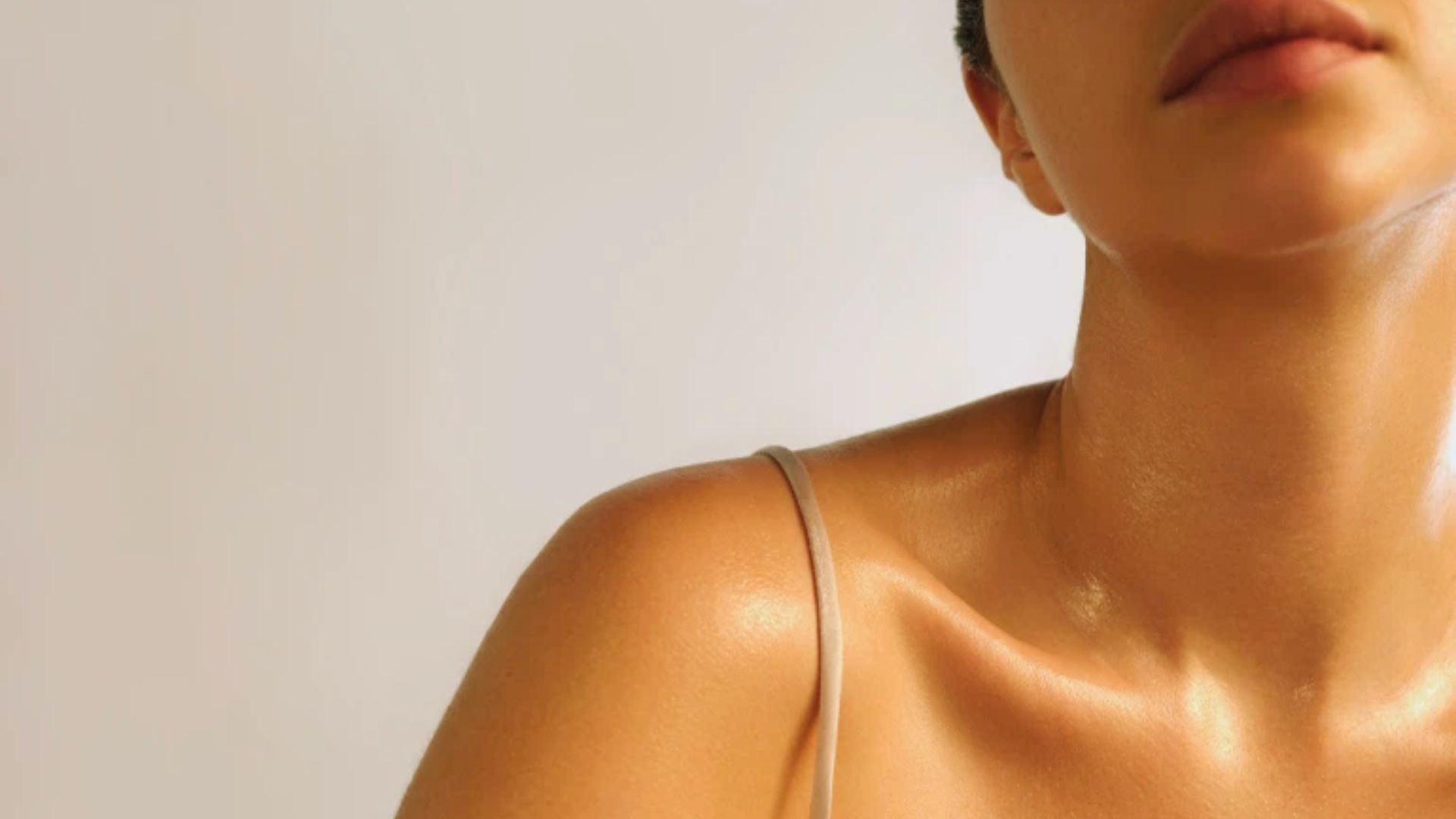 Close-up of a woman's shoulders and neck with dewy skin illuminated by soft light. She wears a thin strap top, evoking a calm, serene mood.