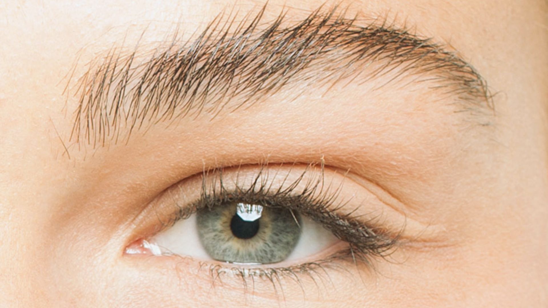 Close-up of an eye with light skin tone, showcasing a green iris, defined eyebrow, and natural lashes. The image conveys an attentive and serene mood.