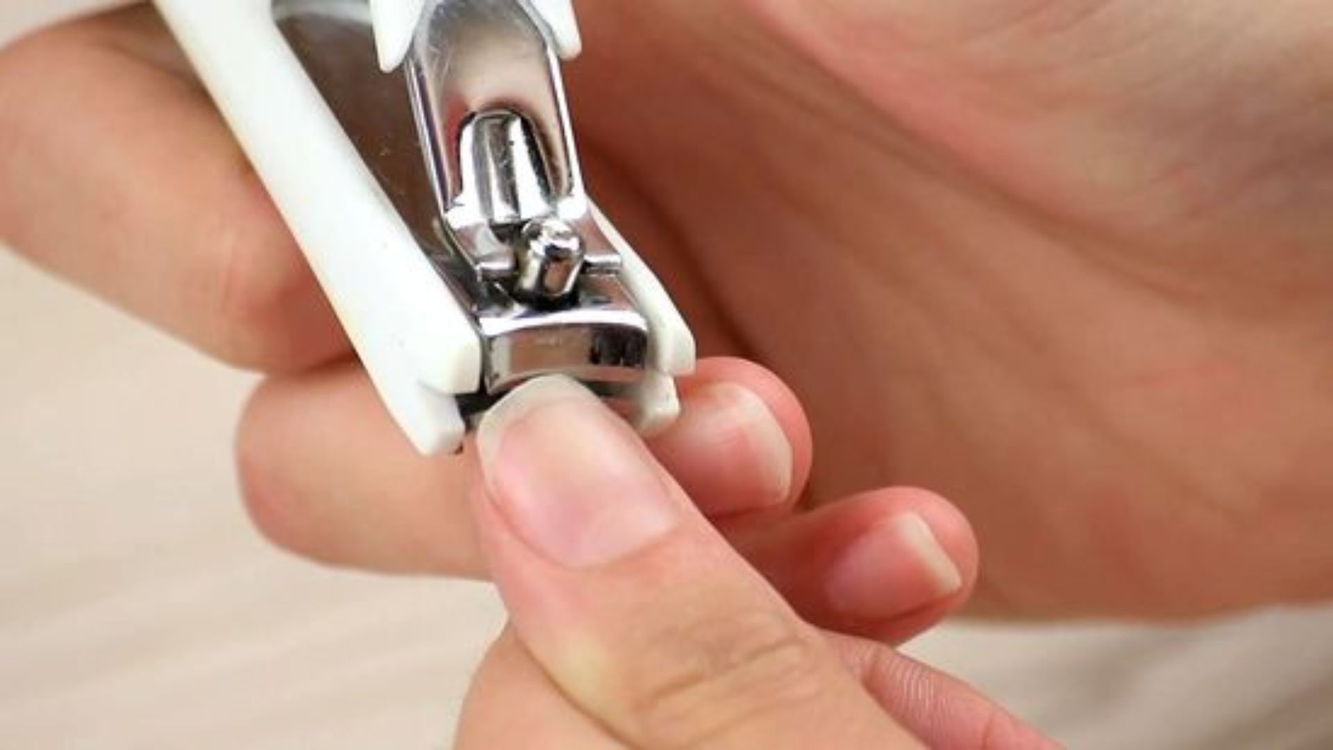 A close-up of hands using a metal nail clipper to trim fingernails. The background is softly blurred, conveying a sense of self-care and grooming.
