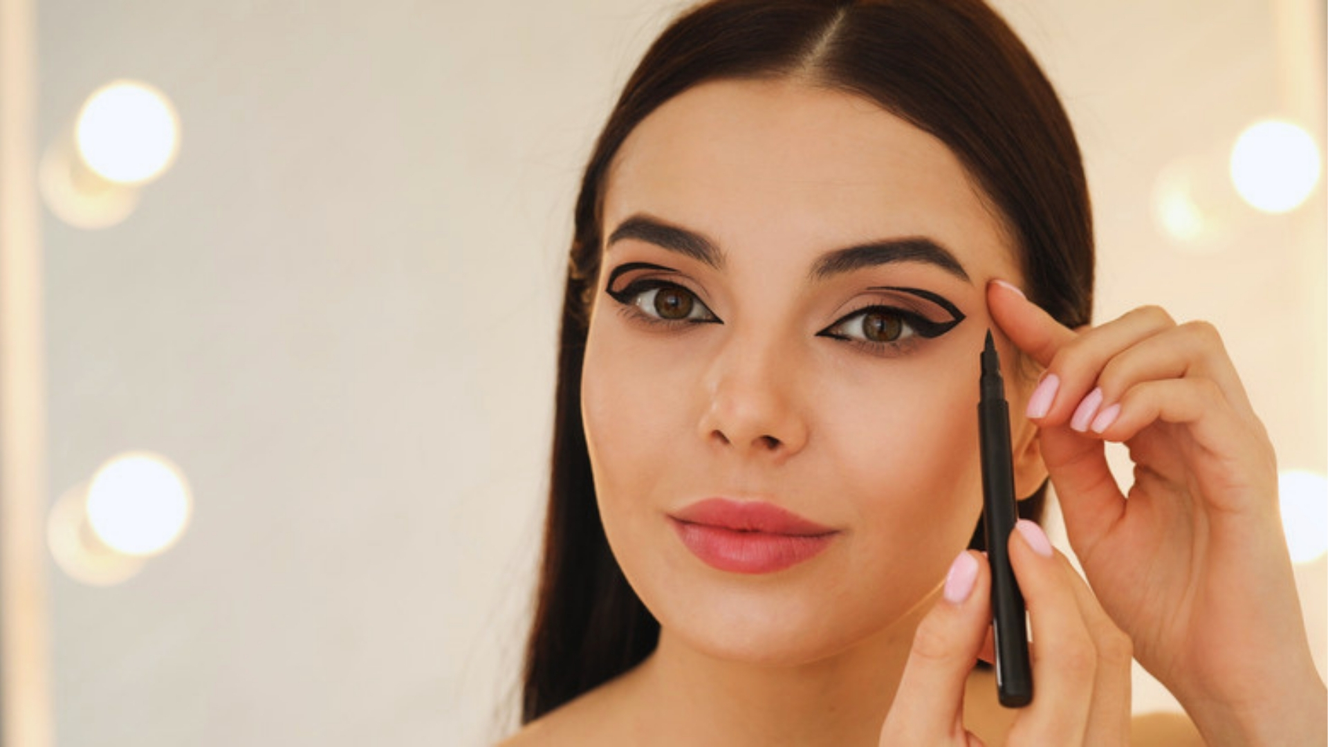 A woman applies liquid eyeliner confidently, showcasing a precise winged look. Her expression is focused, with soft lighting and an elegant tone.