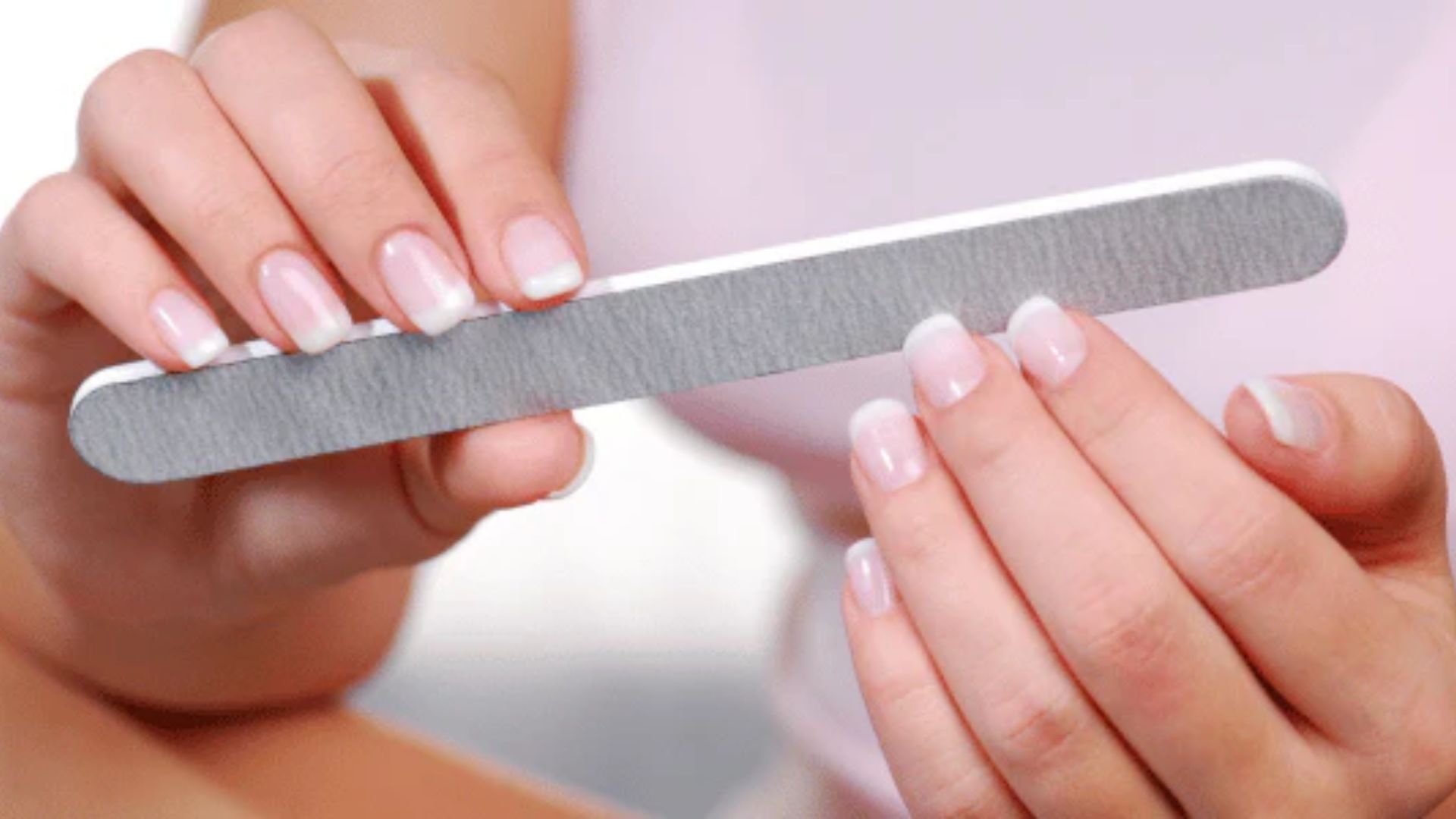 Close-up of hands filing nails with a gray emery board, focusing on nail grooming. The image conveys a sense of care and personal hygiene.