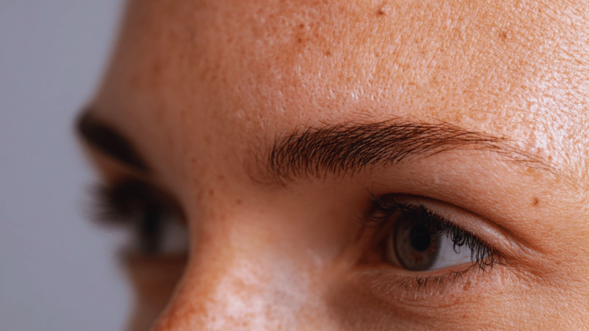 Close-up of a person's expressive eyes and eyebrows, with light freckles visible on the skin. The tone is natural and focused, emphasizing detail and texture.