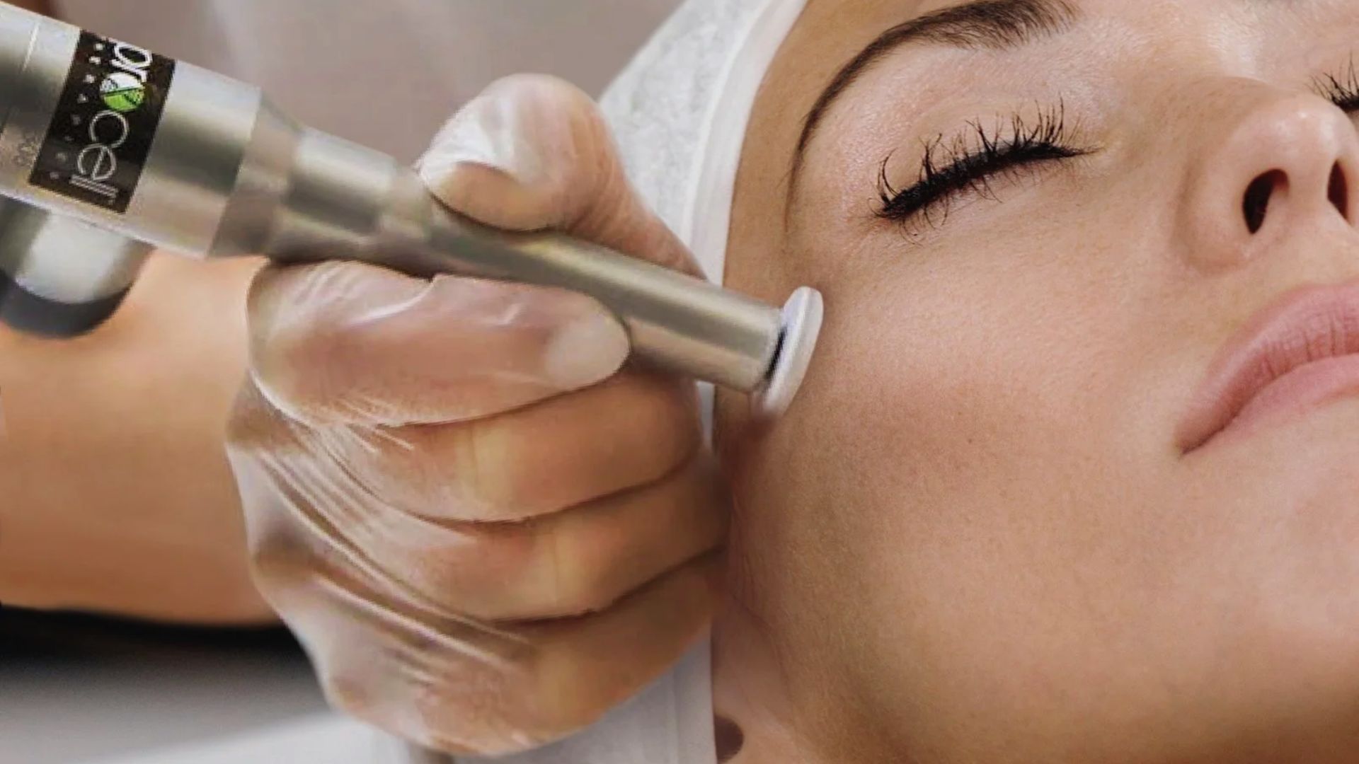 A woman receives a facial treatment with a modern skincare device. A gloved hand gently moves the tool on her cheek, conveying a calm and soothing atmosphere.