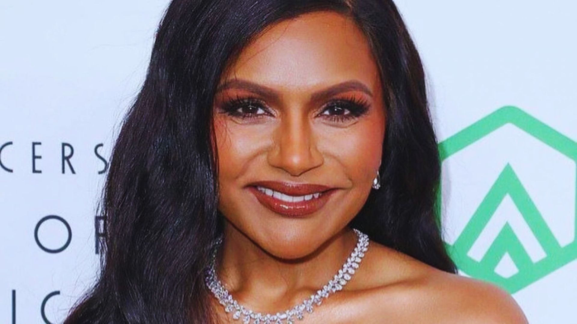 Smiling woman with long, dark hair, wearing an off-shoulder dress and sparkly necklace. Background features minimal text and a green geometric symbol.