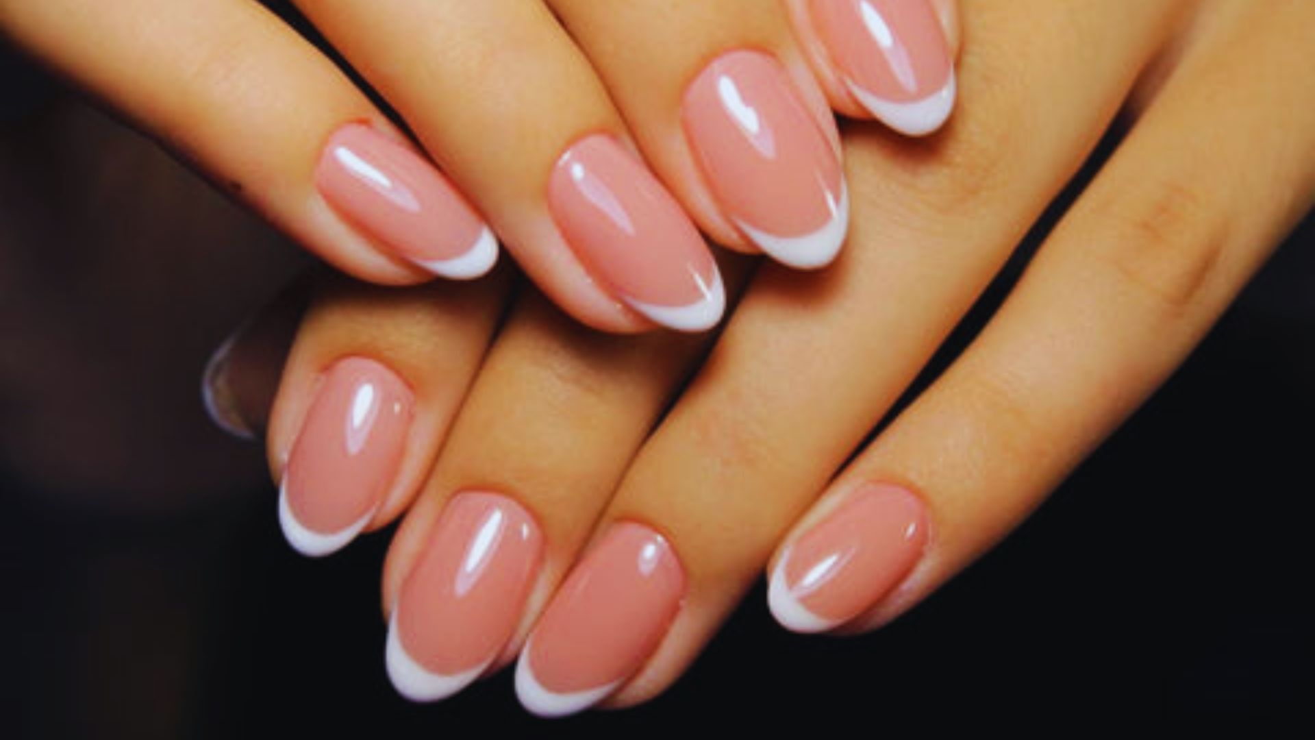 Two hands with a classic French manicure. The nails are glossy with pale pink bases and elegant white tips, conveying a polished and sophisticated look.