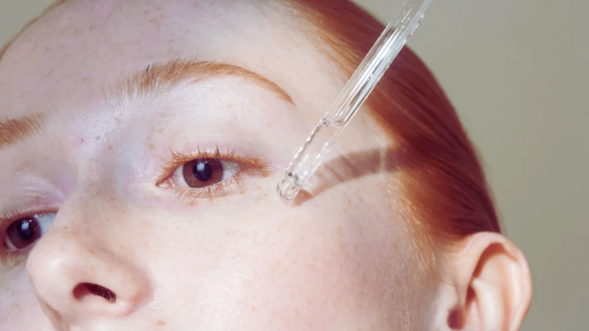 A close-up of a person with fair skin applying serum with a dropper near their eye, showcasing a skincare routine. The tone is soothing and focused.