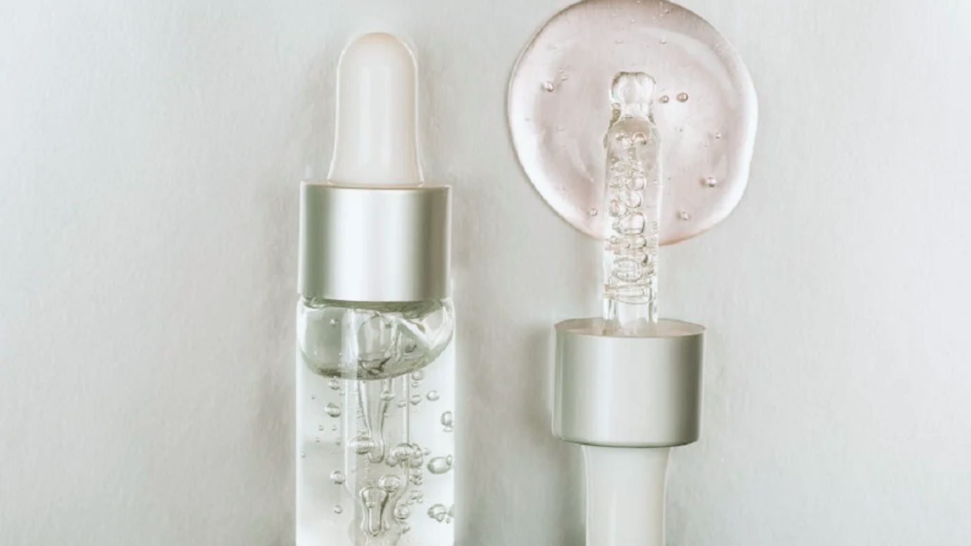 Clear glass dropper bottles with silver lids on a light background. One dropper is open with clear liquid and bubbles, evoking a clean, minimalist feel.