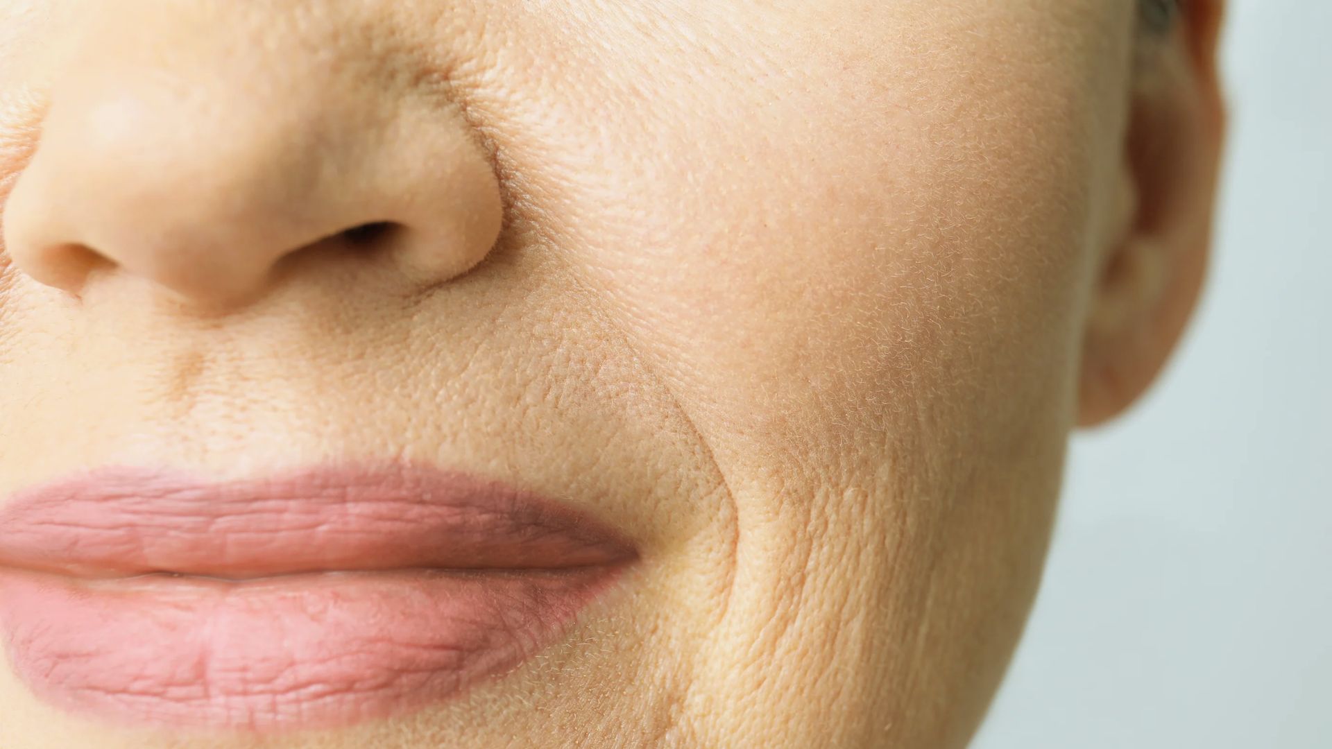 Close-up of a smiling woman's face, focusing on her lips and cheek. The skin shows fine lines and natural texture, conveying warmth and maturity.
