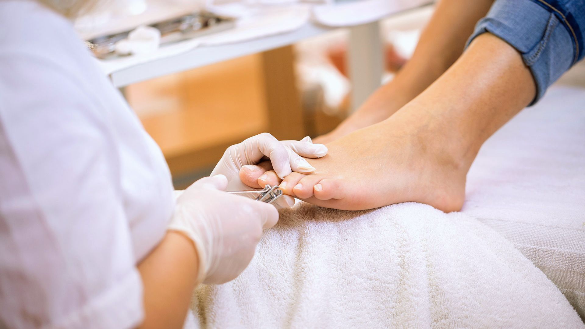 A person receives a pedicure in a salon. Gloved hands trim toenails using clippers on feet resting on a white towel. Calm, hygienic setting.