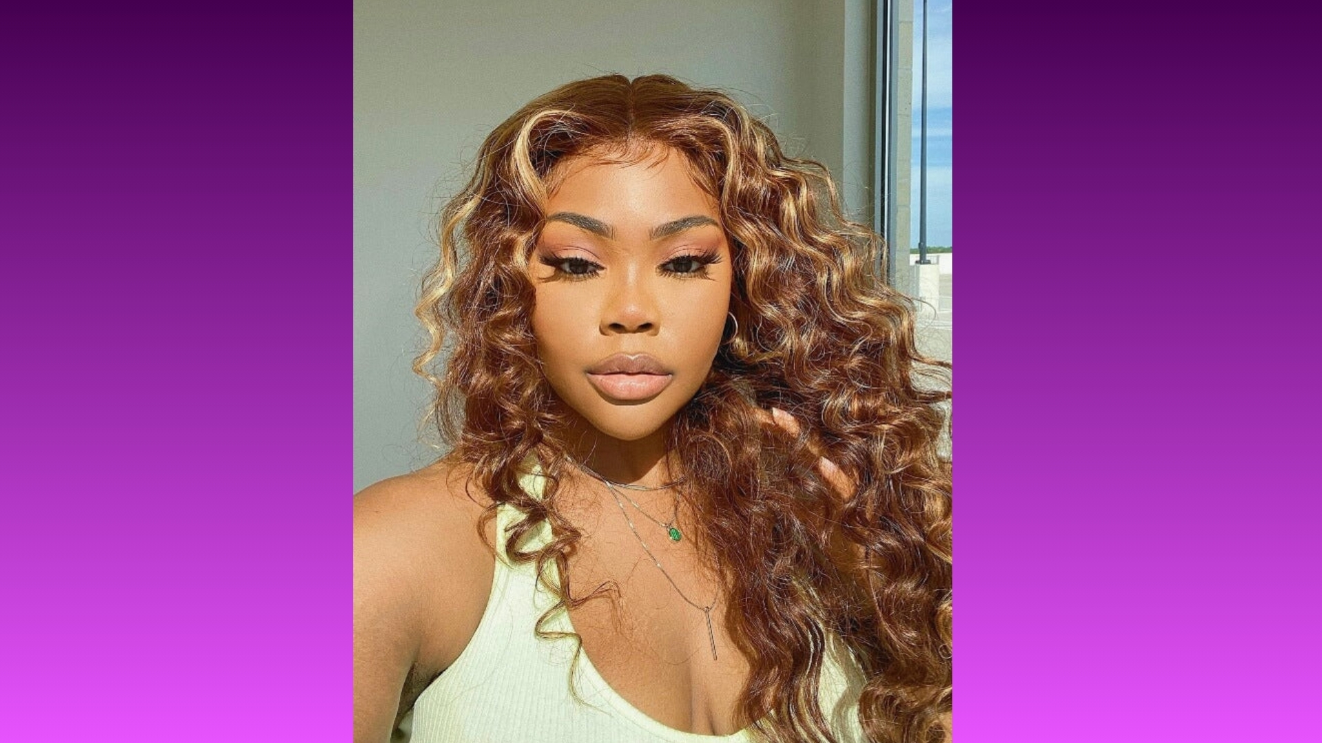 A confident person with long, curly hair poses in front of a blurred window. Wearing a light green top, they convey elegance against a purple gradient background.