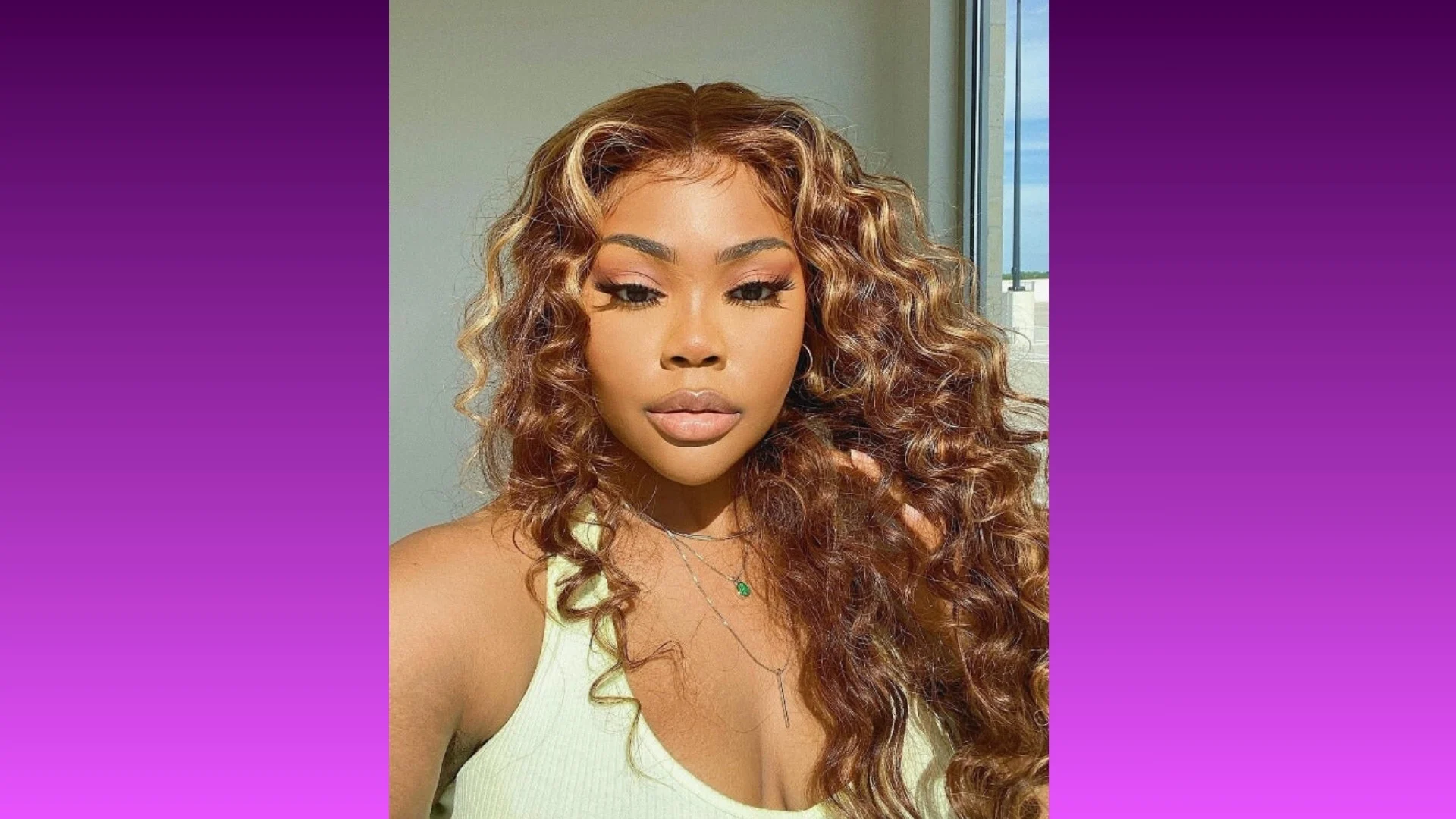 A confident person with long, curly hair poses in front of a blurred window. Wearing a light green top, they convey elegance against a purple gradient background.