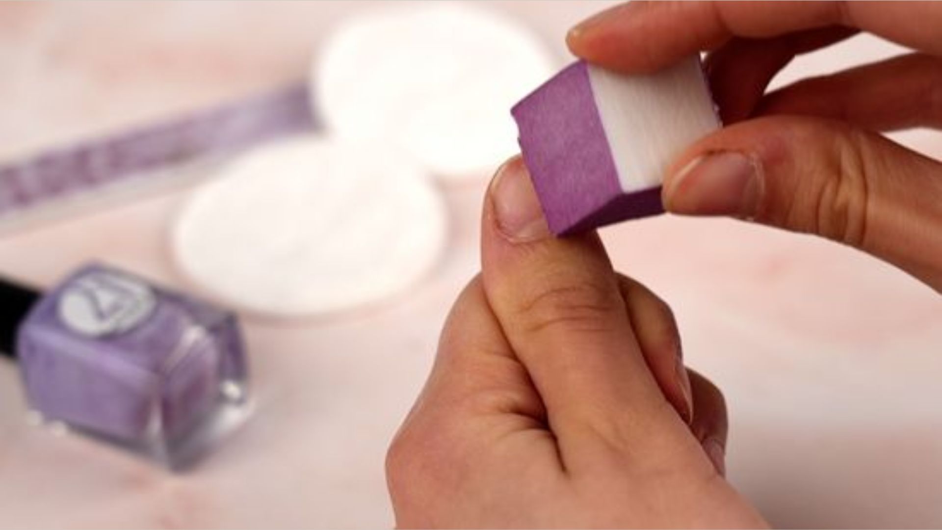 A person uses a purple nail buffer on their thumb, surrounded by nail care items like a file and purple nail polish. The scene feels focused and soothing.