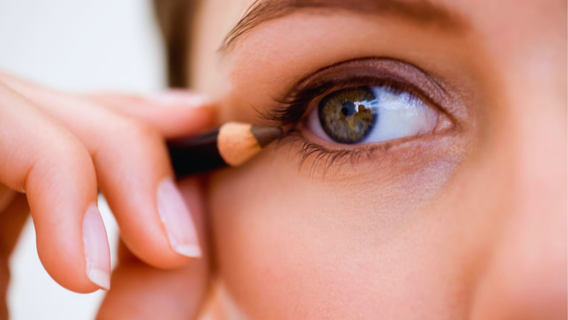 A person applies eyeliner to their upper eyelid, focusing on enhancing the eye. The close-up highlights precision and the eye's natural color.