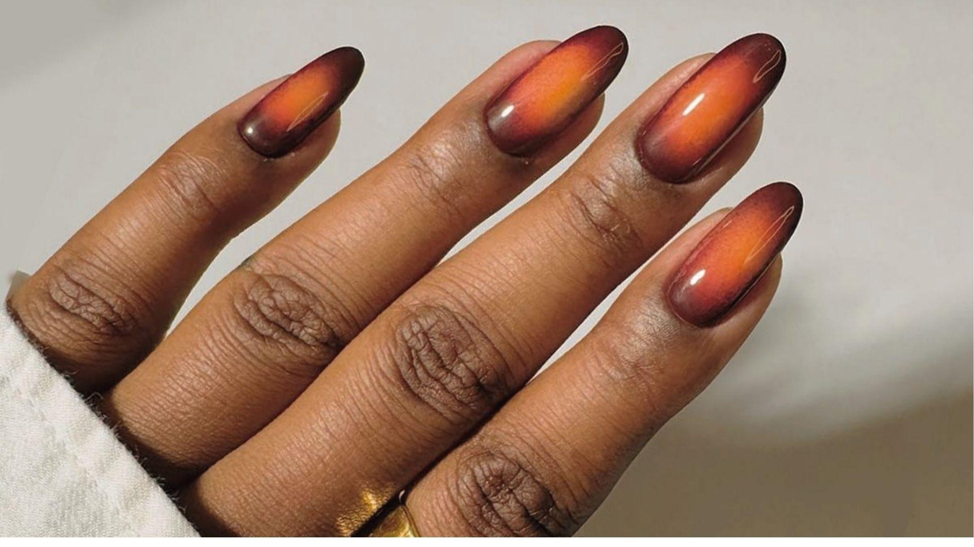 Almond dip nails with glossy sunset aura ombre in deep burgundy fading to bright orange centers.