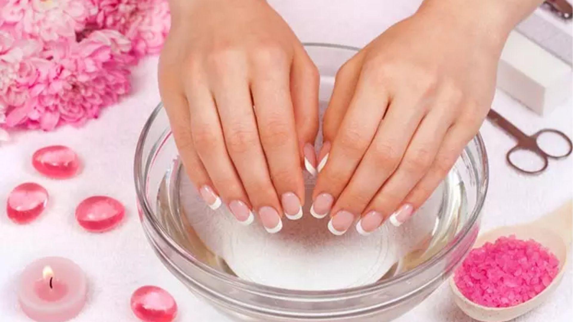 French tip nails soaking in clear bowl with spa items nearby to loosen gel polish with acetone soak