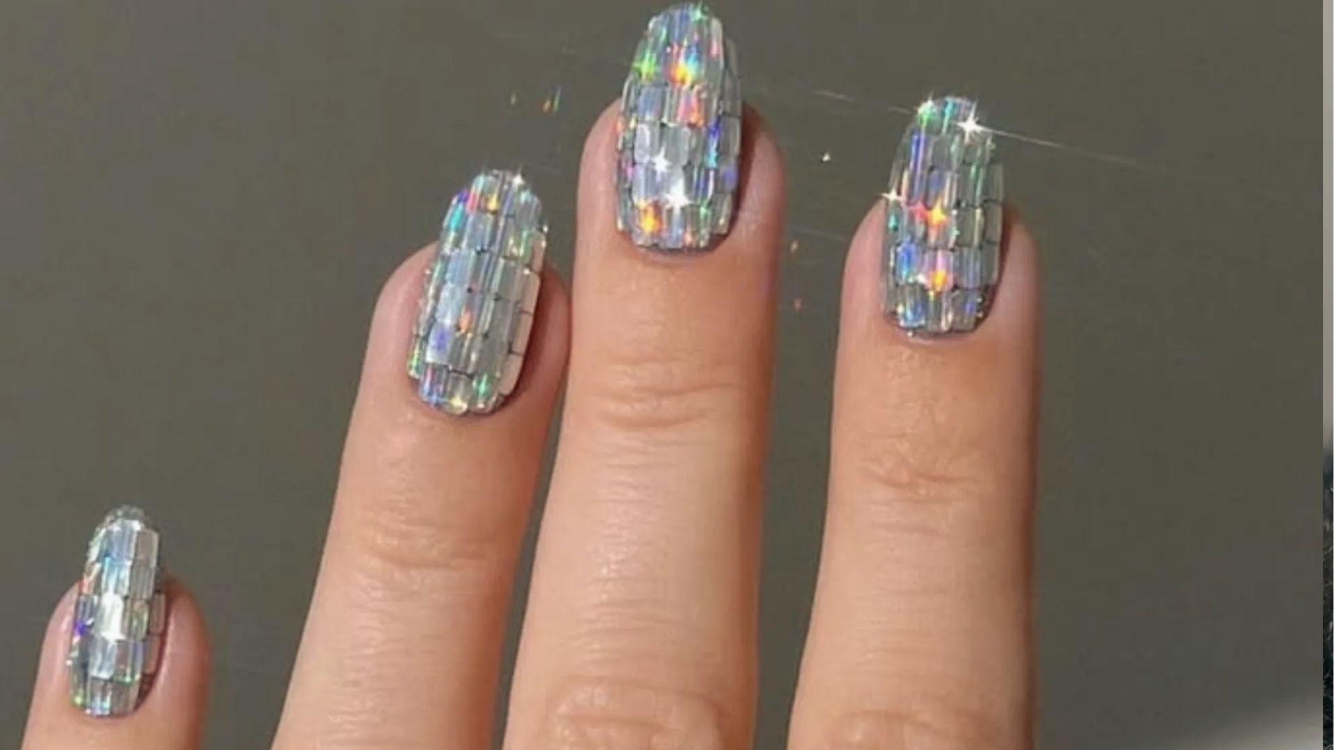 Oval dip nails covered in holographic silver disco ball tiles catching rainbow light for party glam.