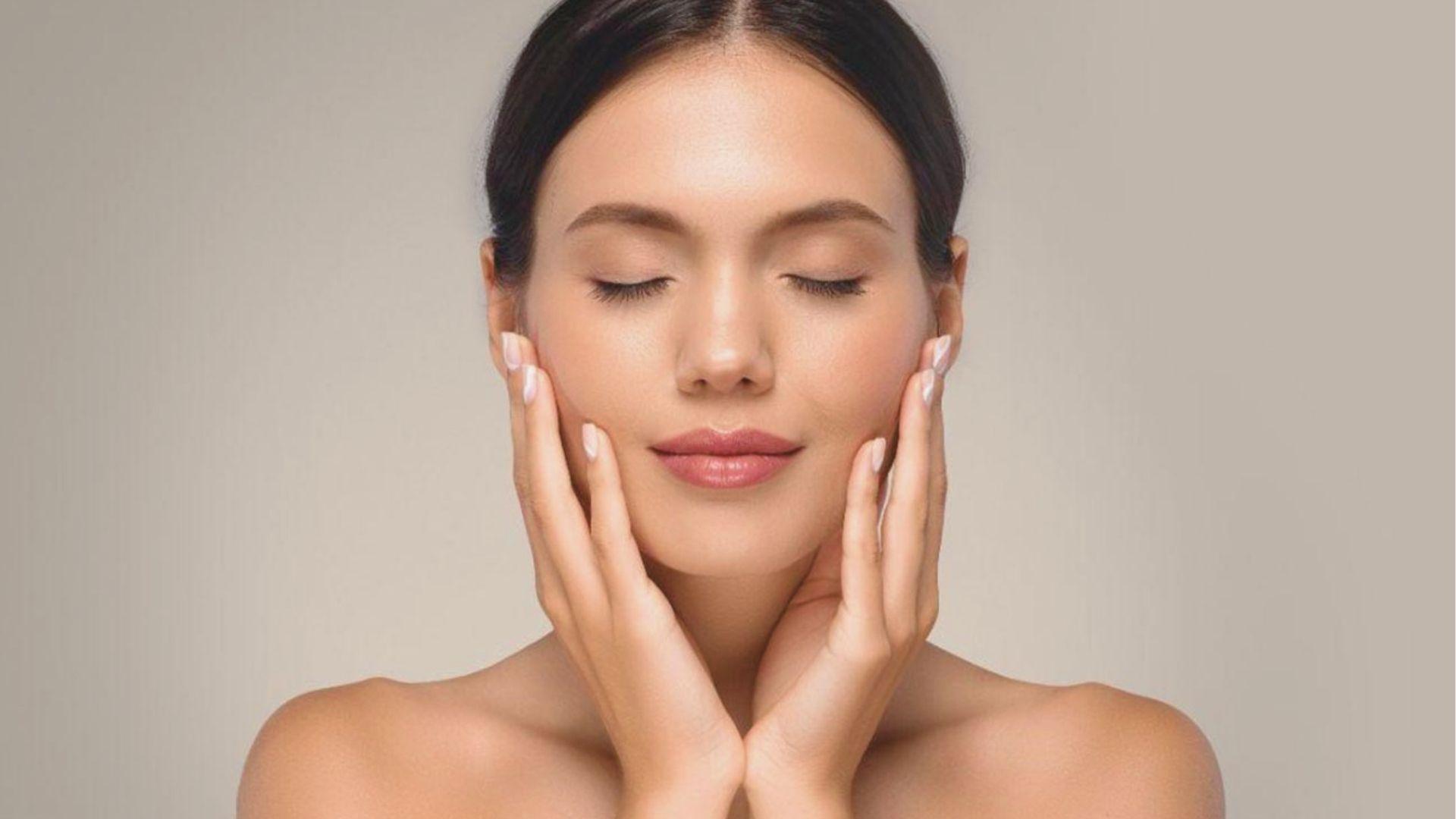 A serene woman with closed eyes and flawless skin holds her face with both hands in a calm pose.