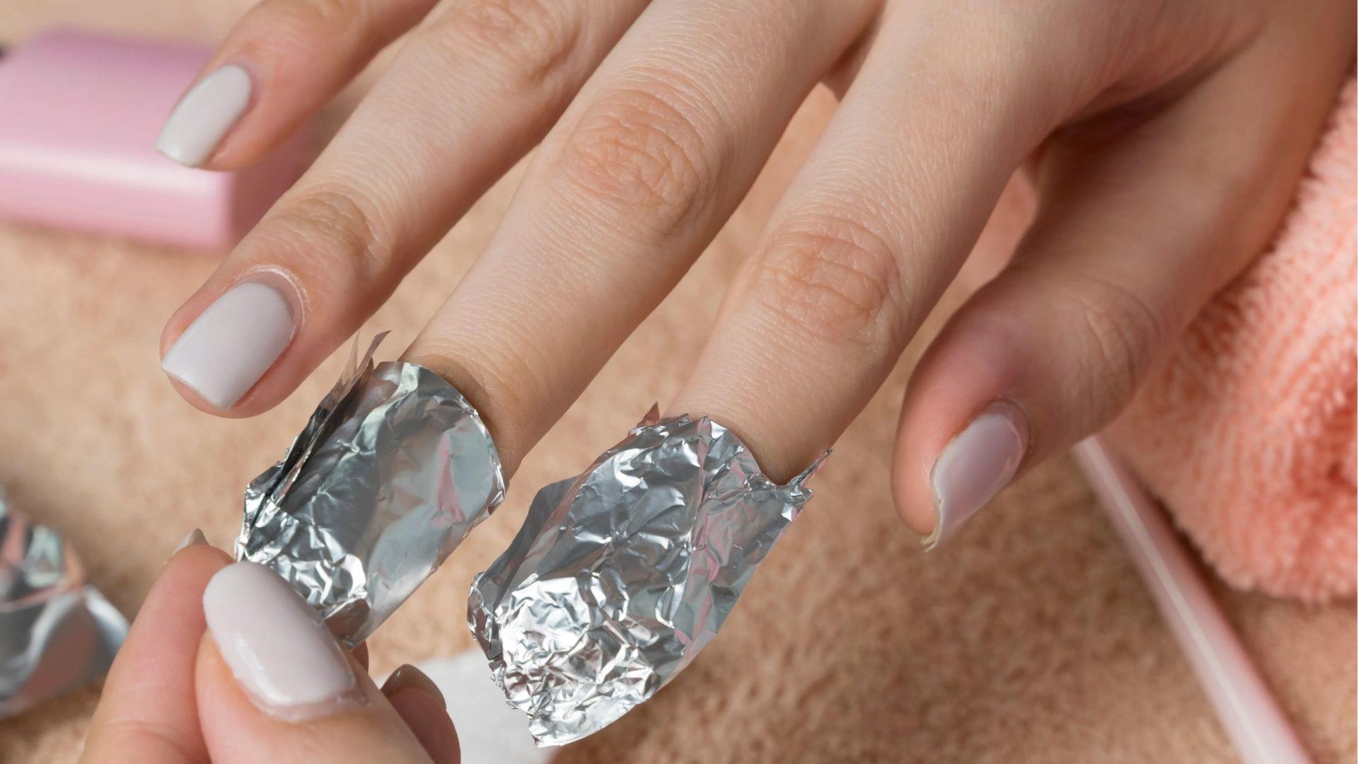 Fingers with white polish wrapped in acetone-soaked foil to break down acrylic nails after 10 minutes