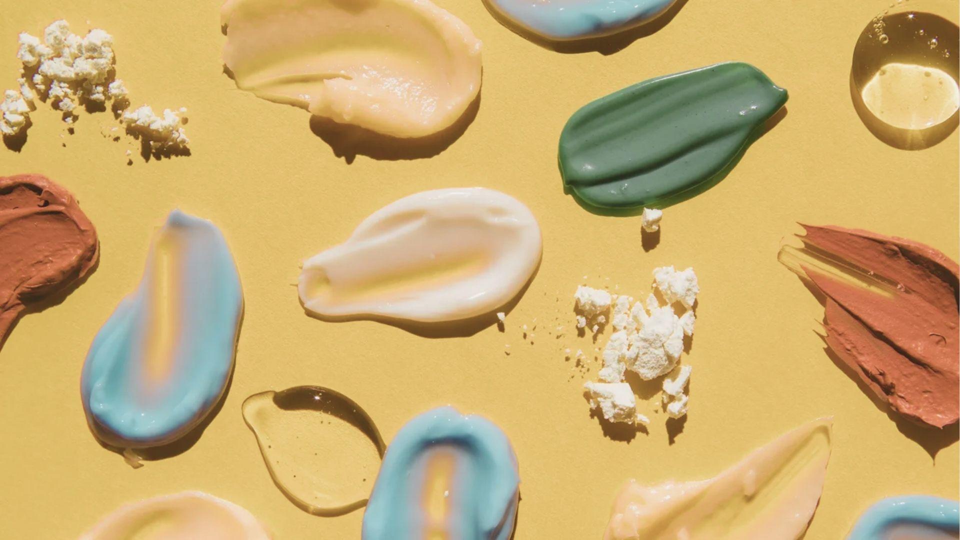 Flat lay of colorful skincare product swatches and textures on a yellow background.