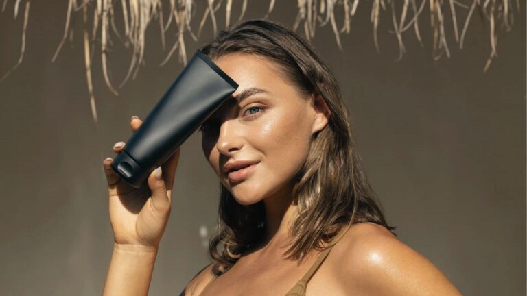 Woman holds black tanning lotion tube in the sun. Bronzers give instant color while DHA develops.