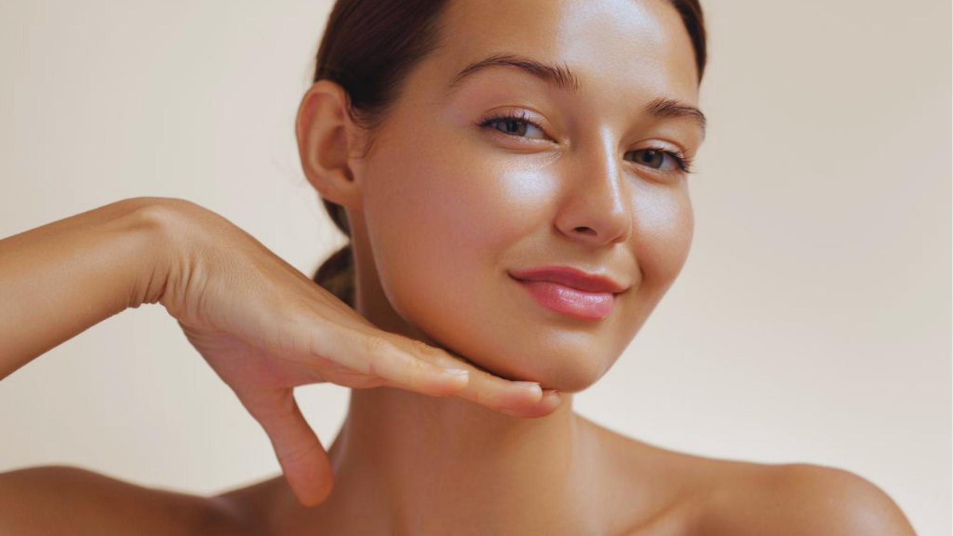 Woman with clear glowing skin smiles while gently framing her face, showing rose oil benefits for healthy skin.