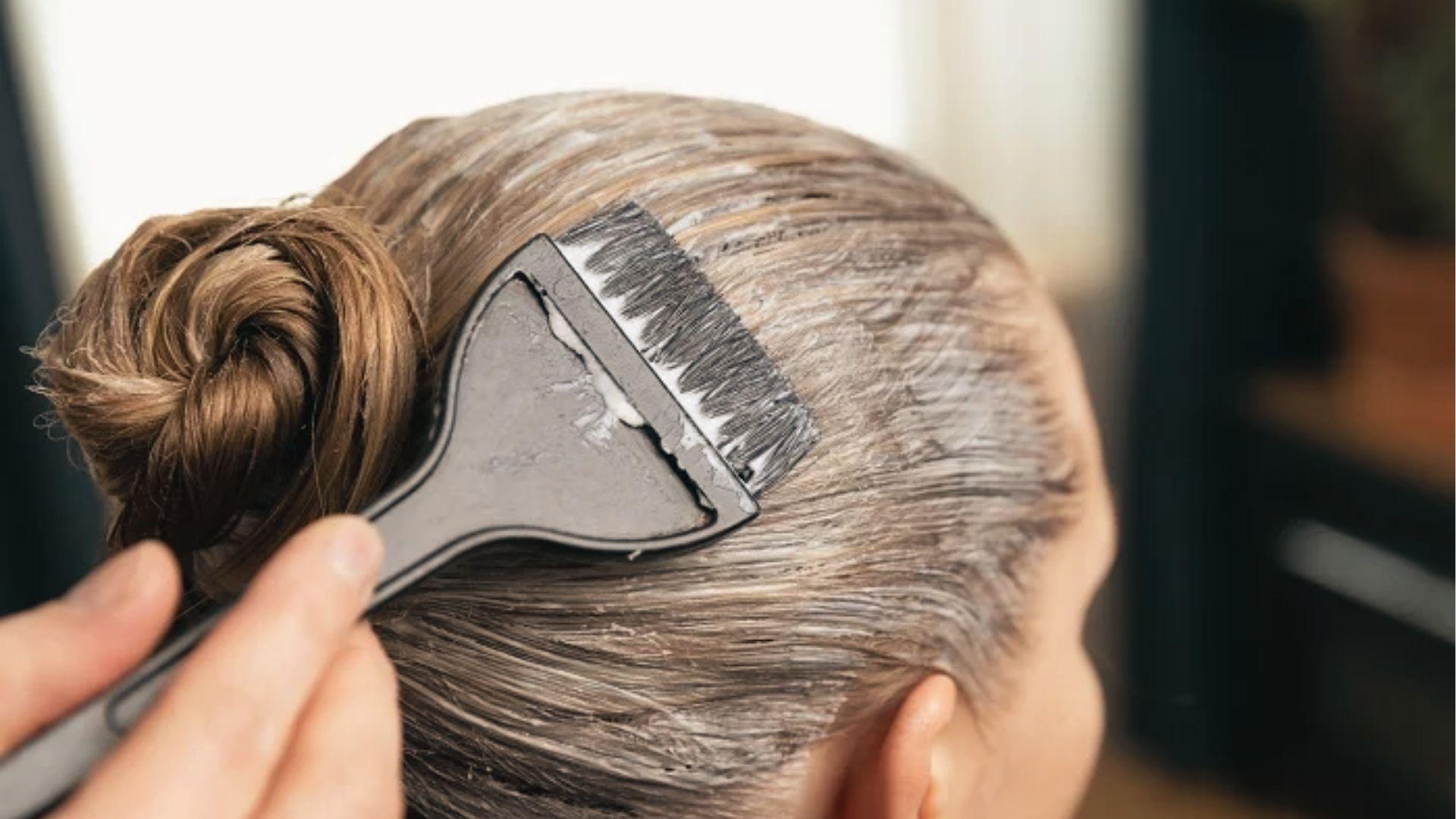 Stylist painting bleach onto blonde hair over foil, monitoring development time for desired shade.