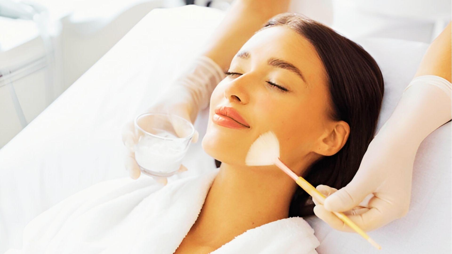 Woman relaxing during facial treatment with brush applying product to reduce acne scars and improve skin texture
