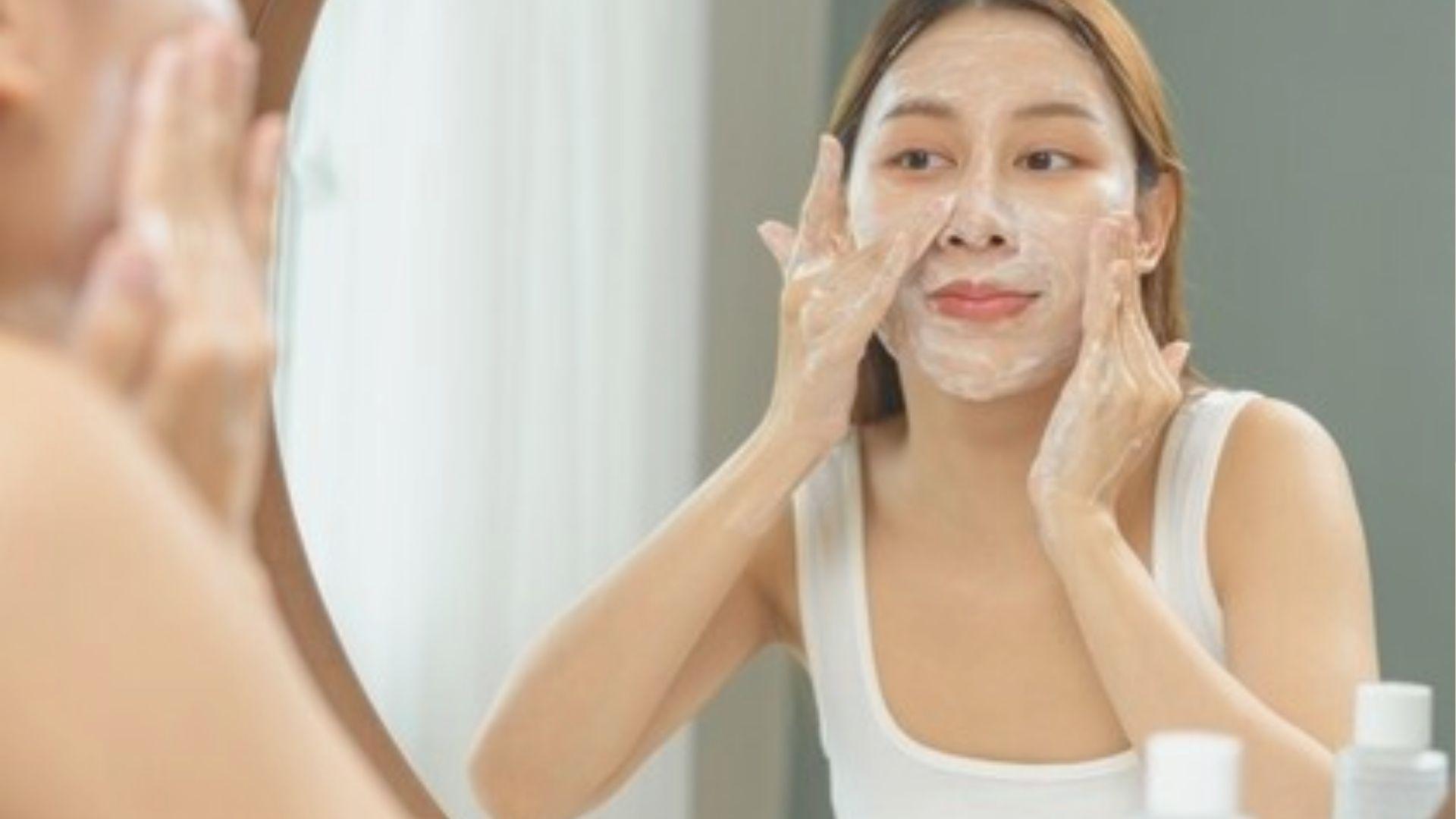 Woman gently cleanses her face with foam in front of a mirror, starting her nighttime skincare routine.