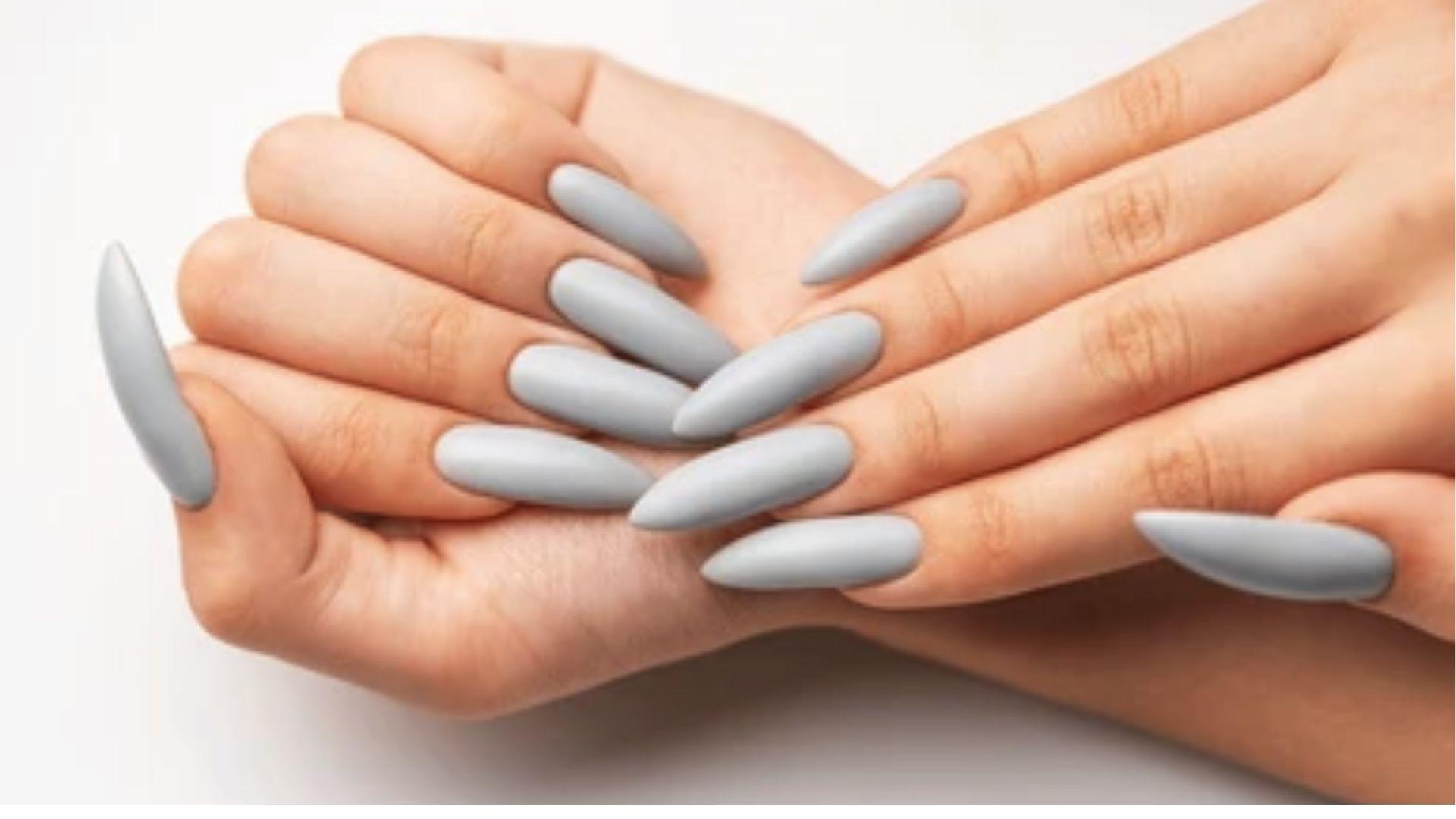 Long almond dip nails in matte light grey finish on both hands crossed against a plain white backdrop.