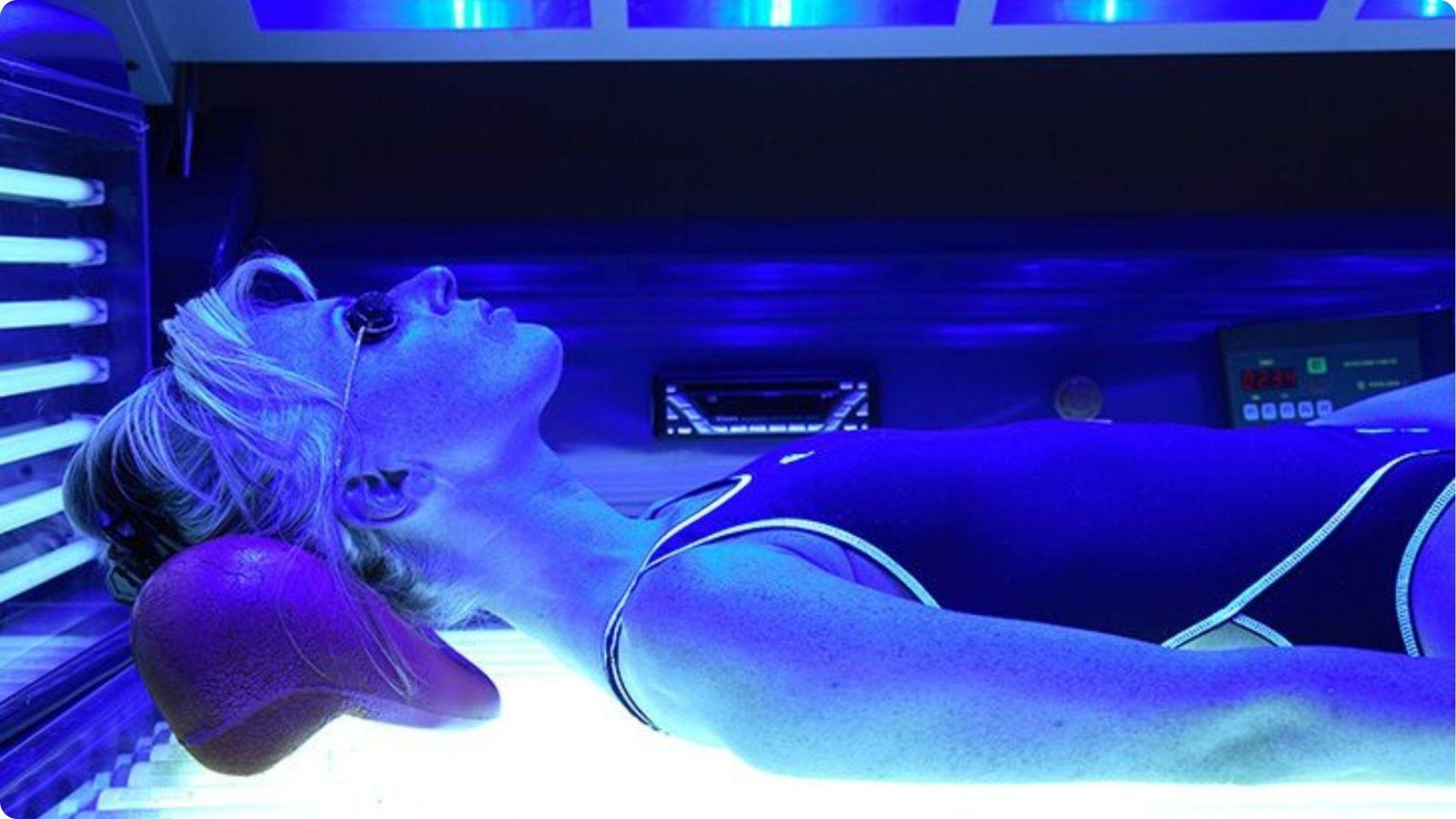 Side view of a woman wearing eye protection while tanning under blue UV lights.