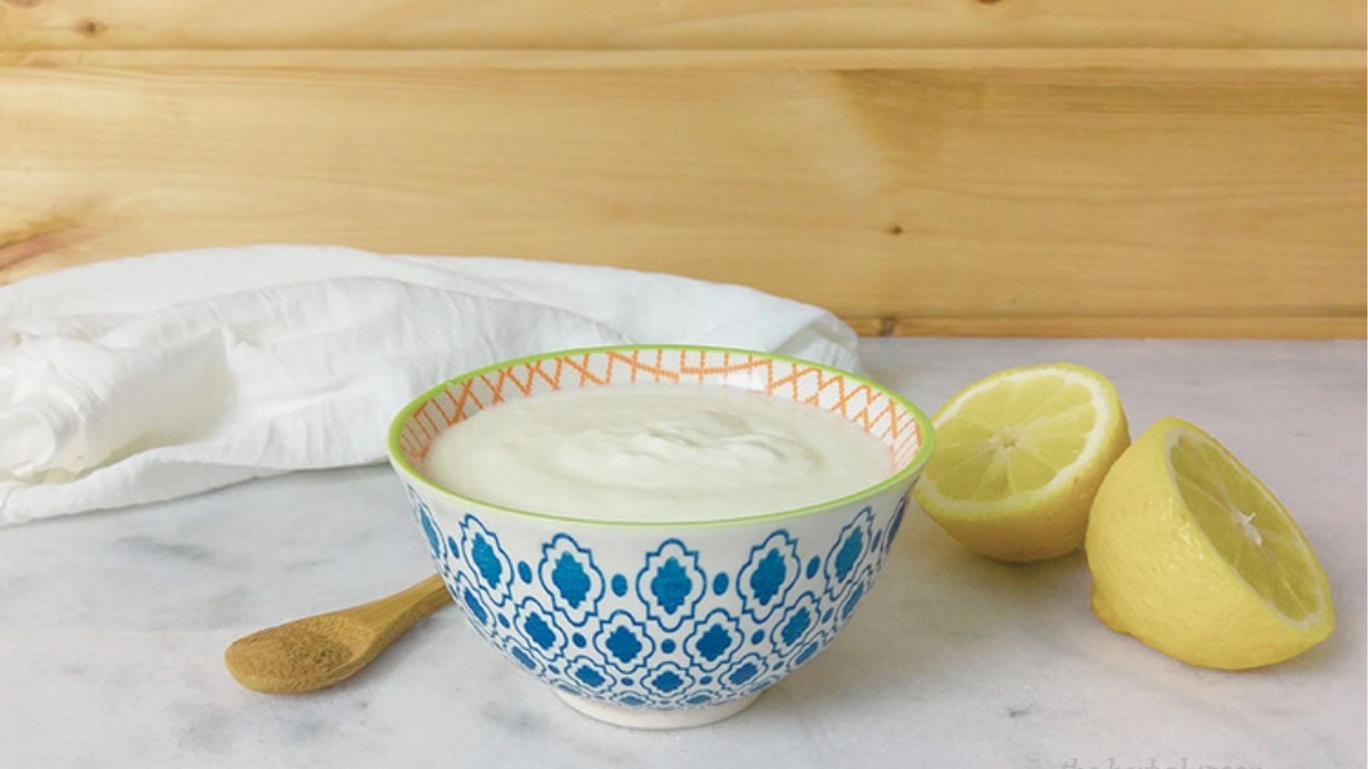 A patterned bowl of fresh yogurt placed next to halved lemons on a marble surface.