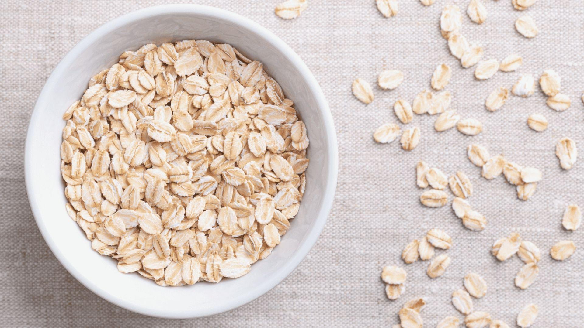 A white bowl filled with raw rolled oats on a linen cloth, ready for a DIY skincare blend.