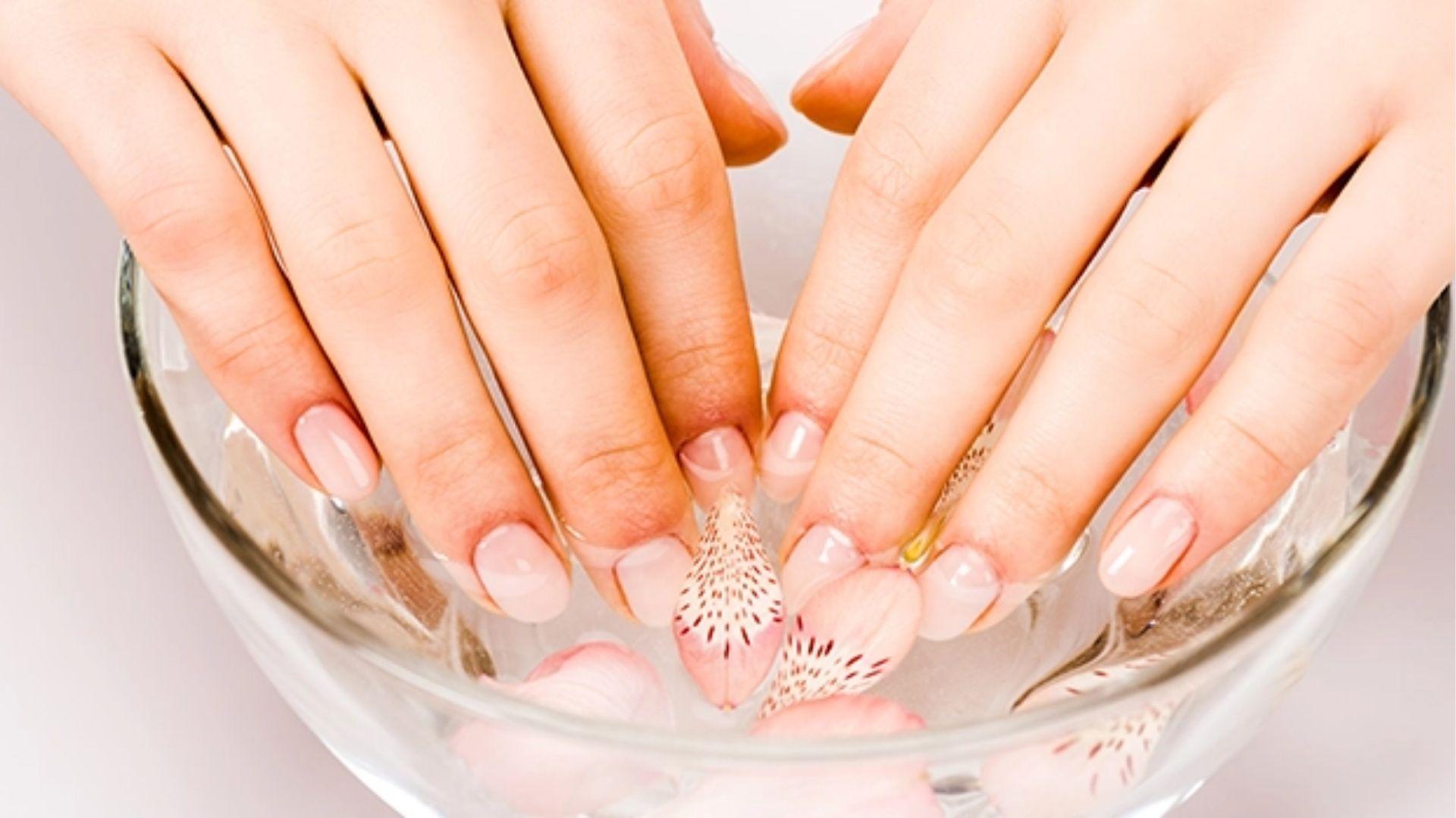 Natural nails submerged in glass bowl with flower petals to soak off gel polish with acetone at home