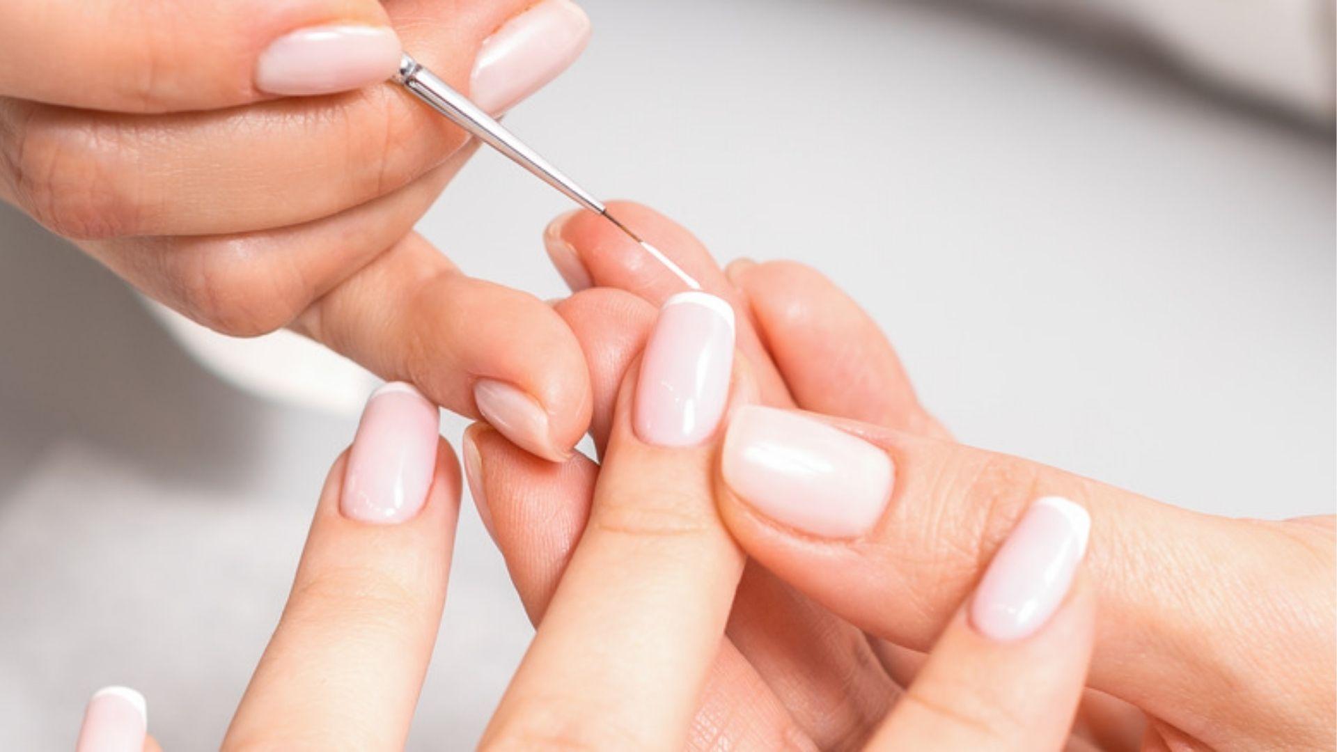 Nail tech paints white tips on natural nails for solar nails, a durable acrylic French style.