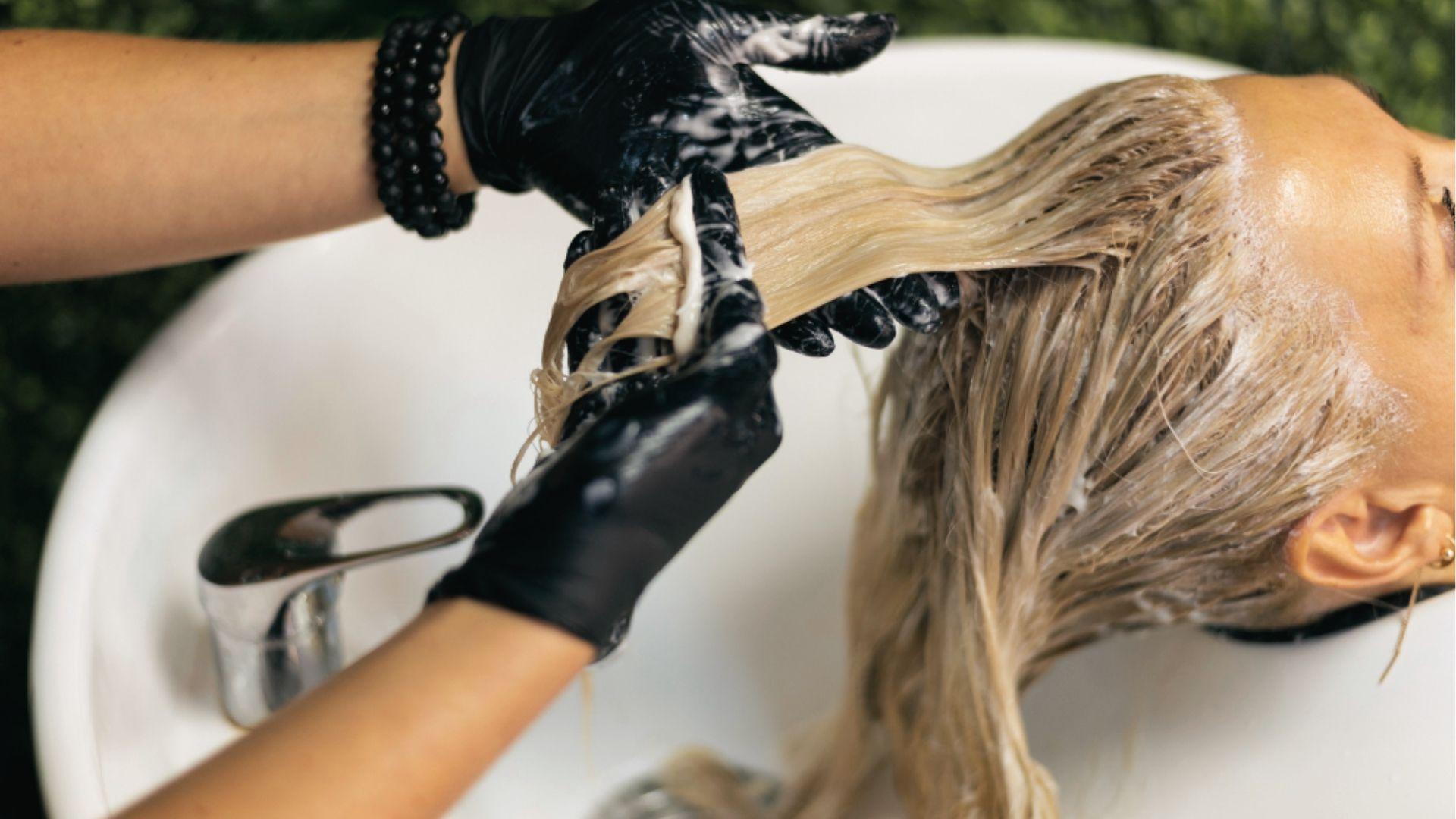 Comb running through bleached, wet hair to distribute product evenly for consistent lift timing.