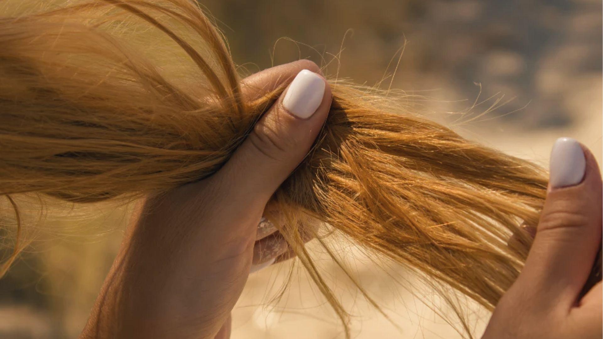Hands holding brassy, damaged hair strands after bleaching to check timing and avoid over-processing.