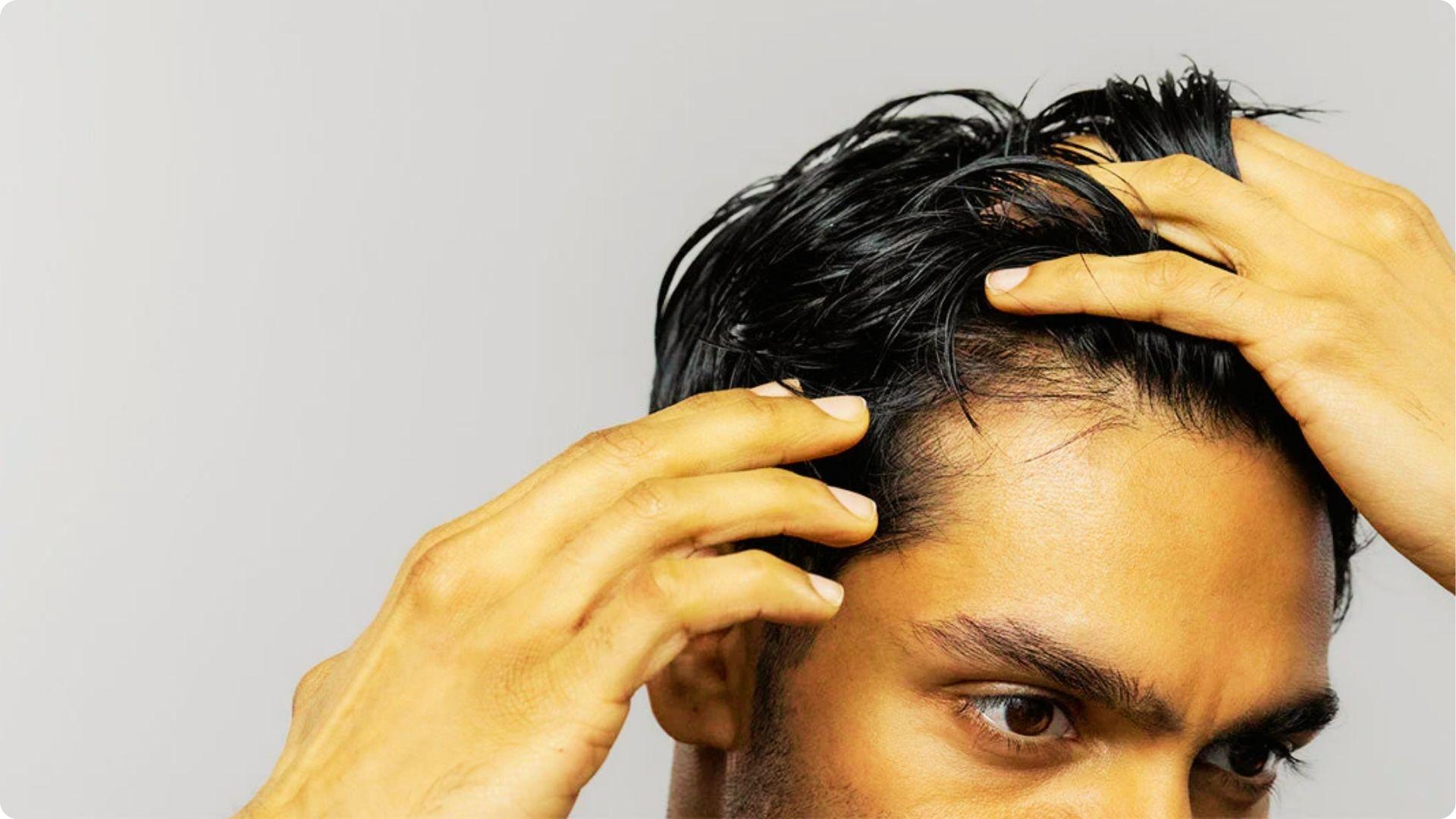 Man lifting wet hair to examine his temple area, showing uneven hair density.