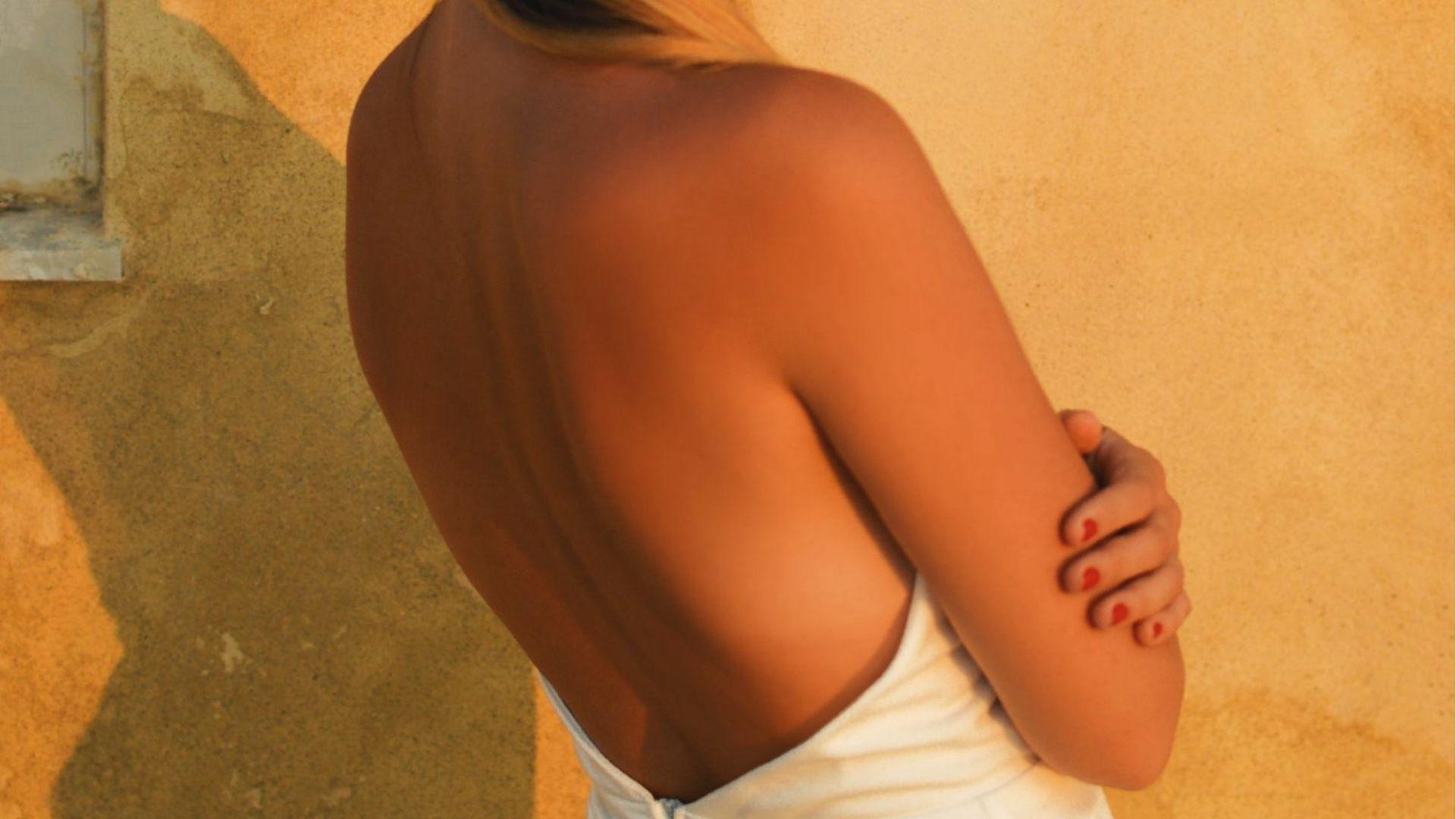 Woman with sun-kissed back and arm showing even golden tan on fair skin in warm sunlight