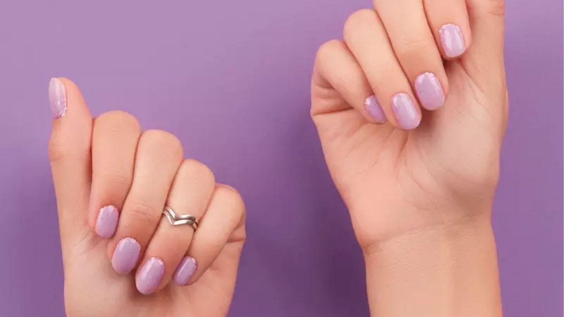 Short oval dip nails in glossy soft lavender on both hands against a matching purple background.