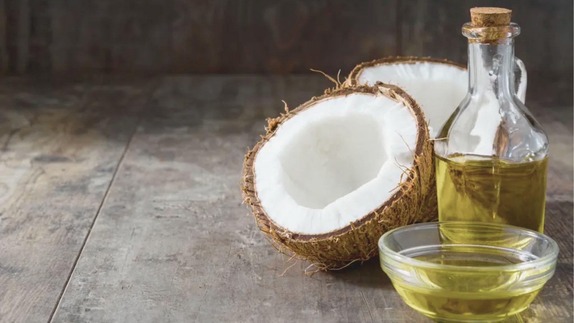 Cracked coconut, glass bottle of oil, and a small bowl of coconut oil on a rustic wooden table.